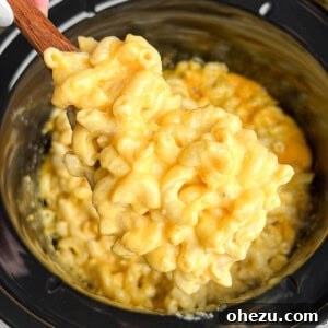 A serving spoon scooping creamy mac and cheese out of a slow cooker.