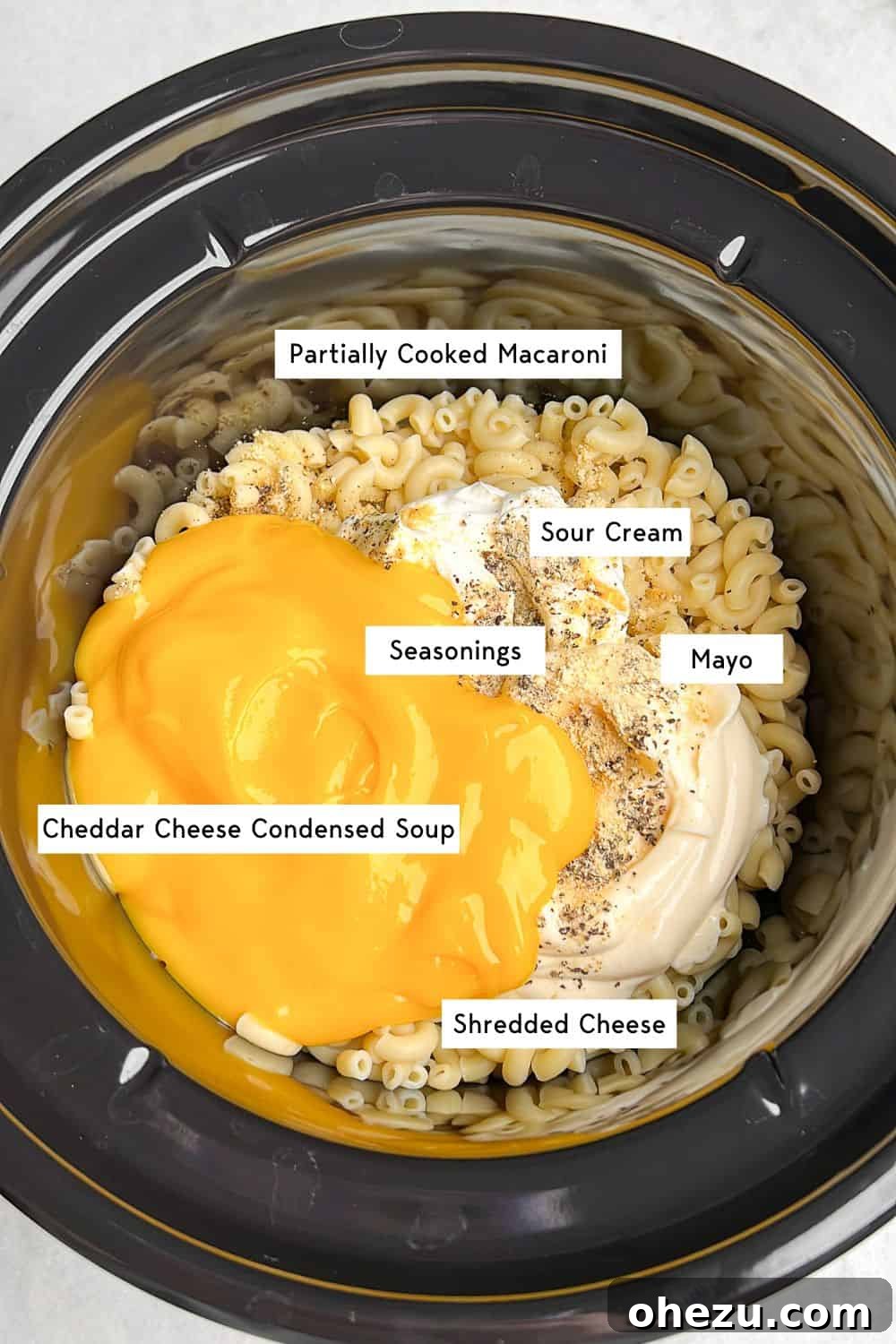 All key ingredients for slow cooker mac and cheese, including pasta, cheese blocks, sour cream, and condensed soup, arranged attractively inside a slow cooker before mixing.