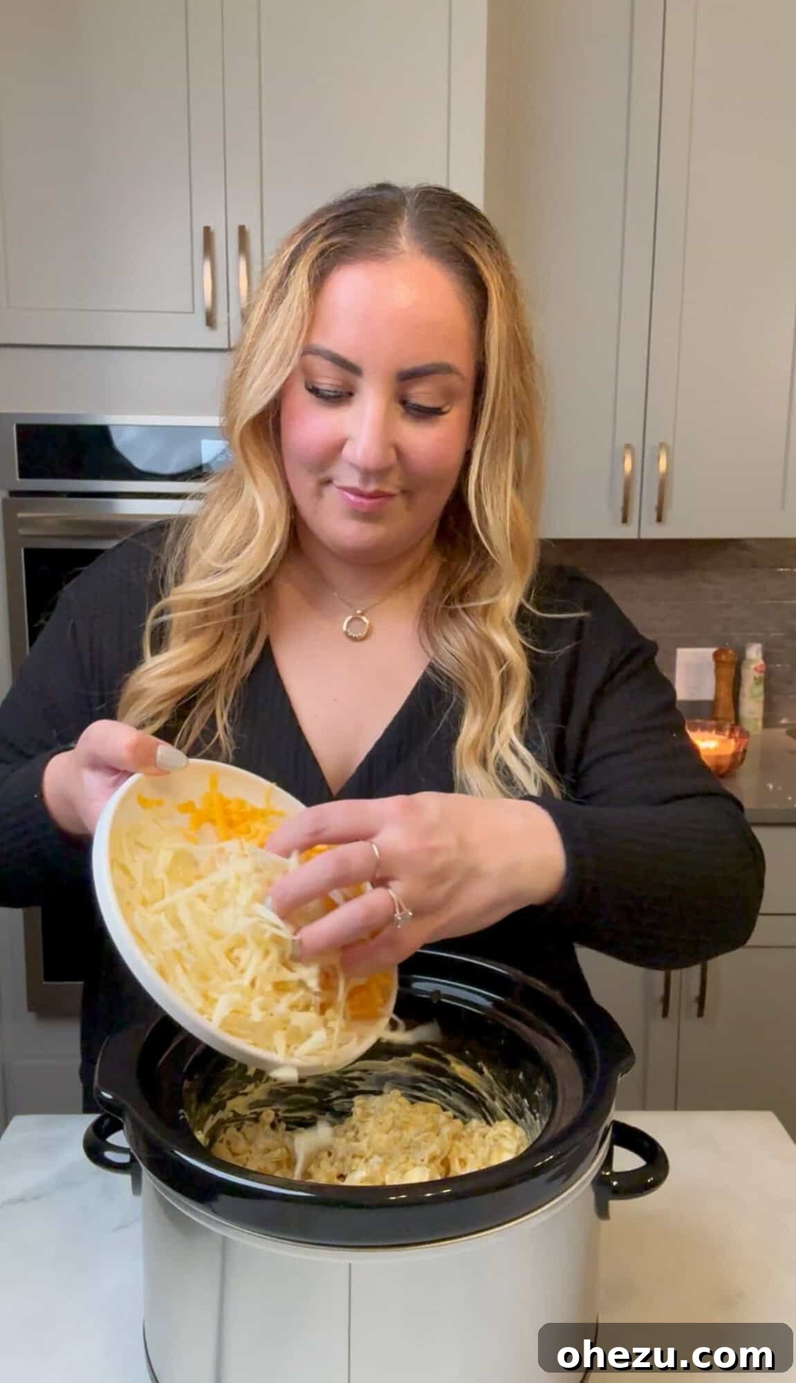A generous sprinkling of additional shredded cheese being added to the top of the bubbling mac and cheese in the slow cooker.