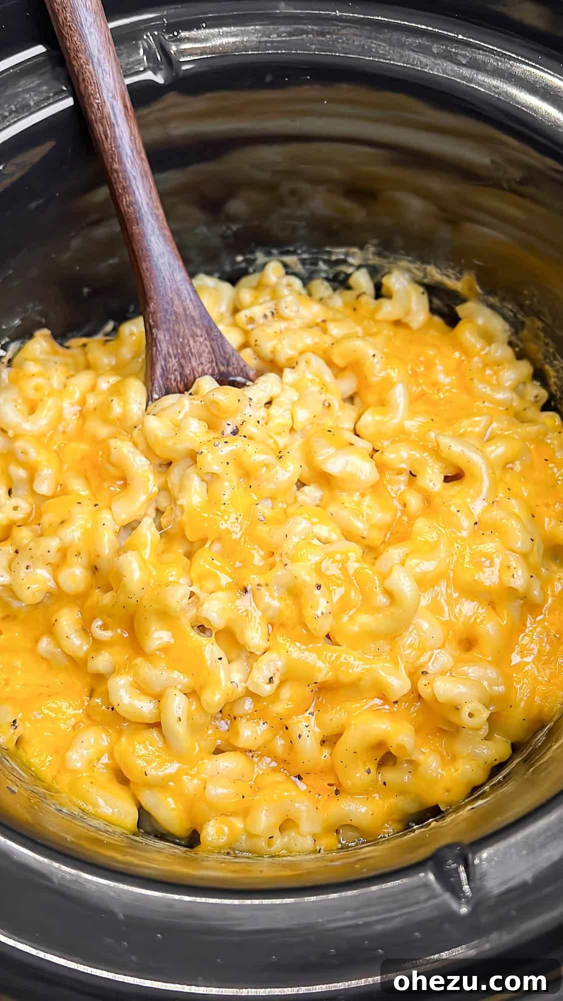 Rich, creamy slow cooker mac and cheese fills the entire slow cooker, with a wooden spoon resting inside, ready for serving.