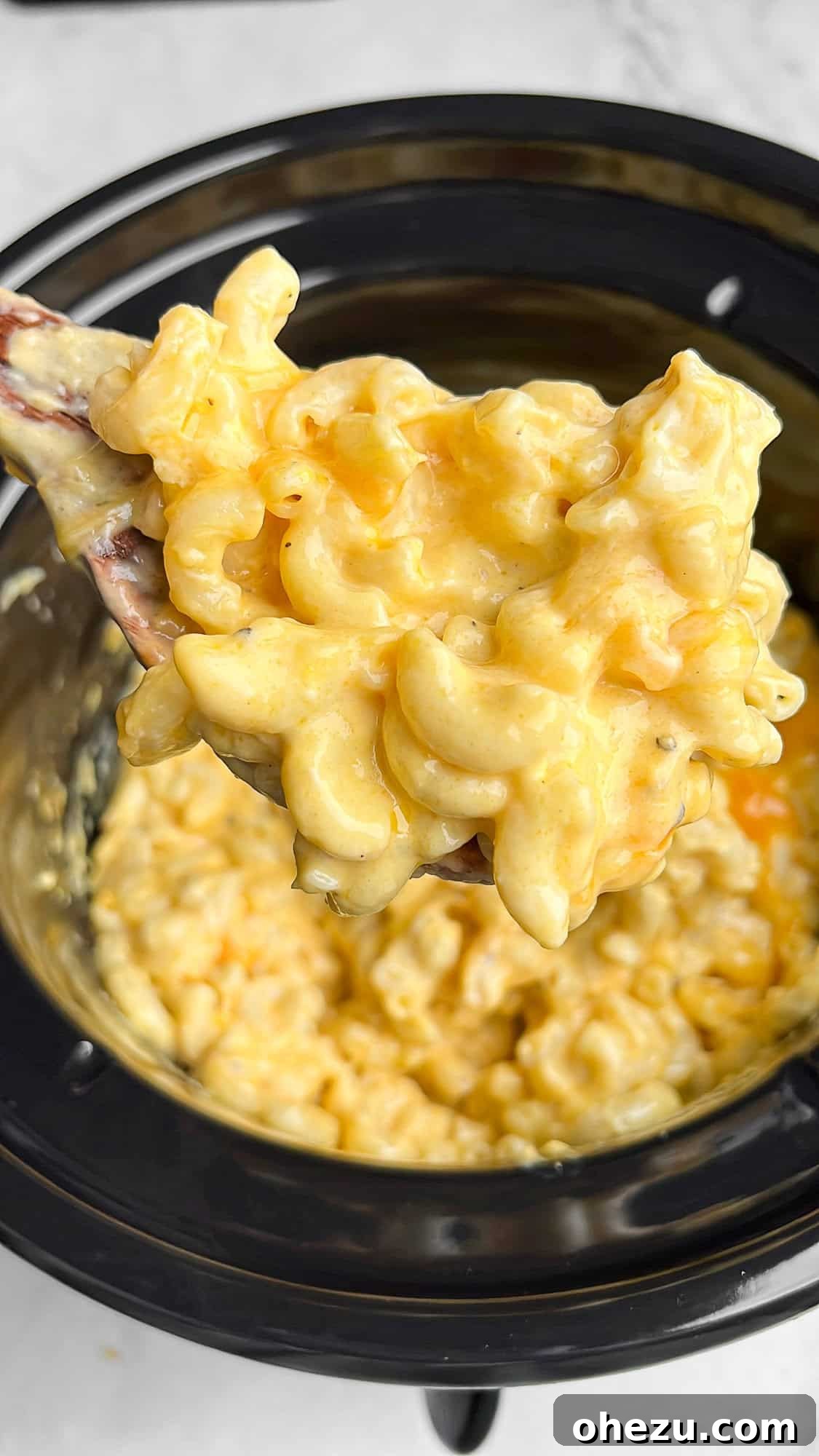 A wooden spoon lifting a generous portion of incredibly creamy, golden slow cooker mac and cheese from the pot, ready to be served.