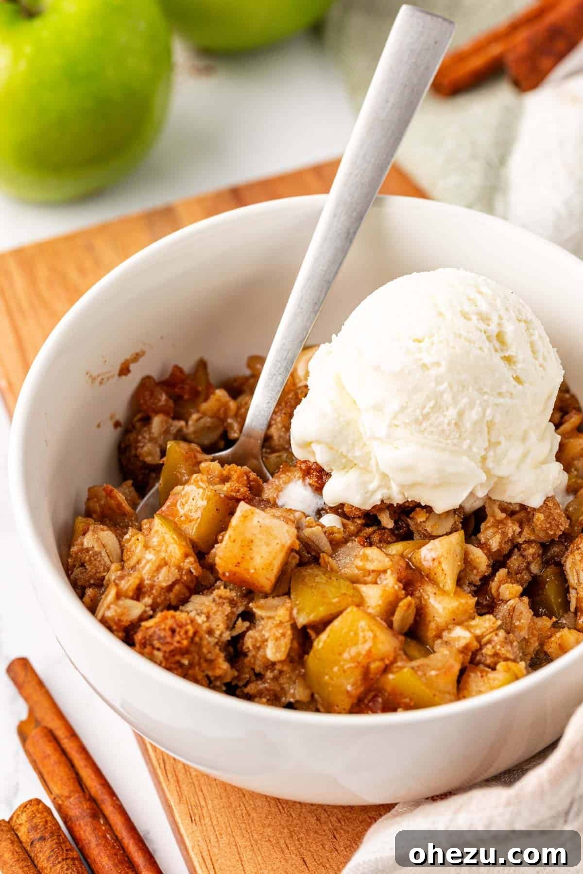 Heavenly Gluten-Free Apple Crumble 17 A close-up shot of a single serving of gluten-free apple crisp in a white bowl, topped with a scoop of vanilla ice cream, garnished with a sprinkle of cinnamon.