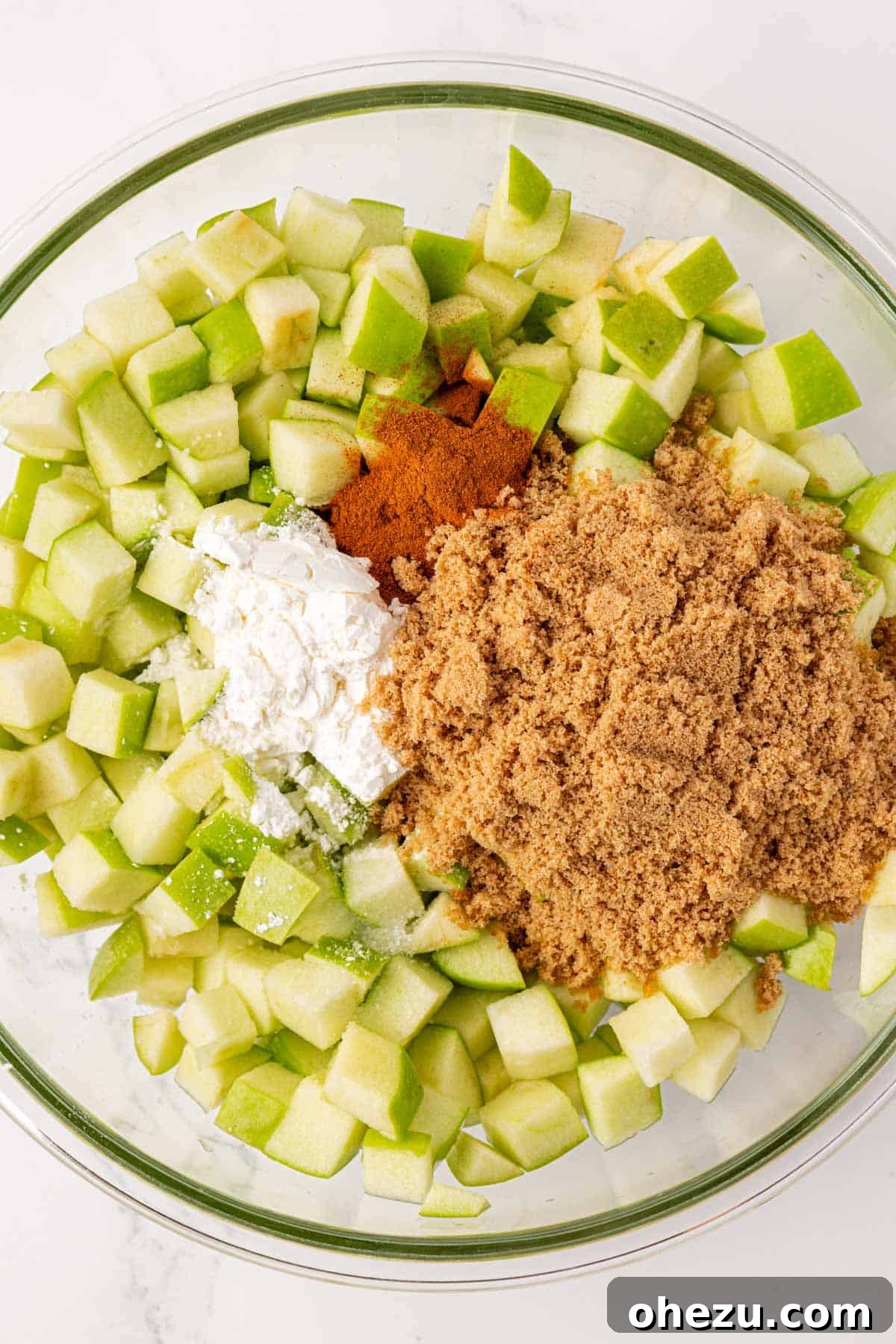 Heavenly Gluten-Free Apple Crumble 7 Spices and brown sugar being sprinkled over diced apples in a mixing bowl for the apple crisp filling.