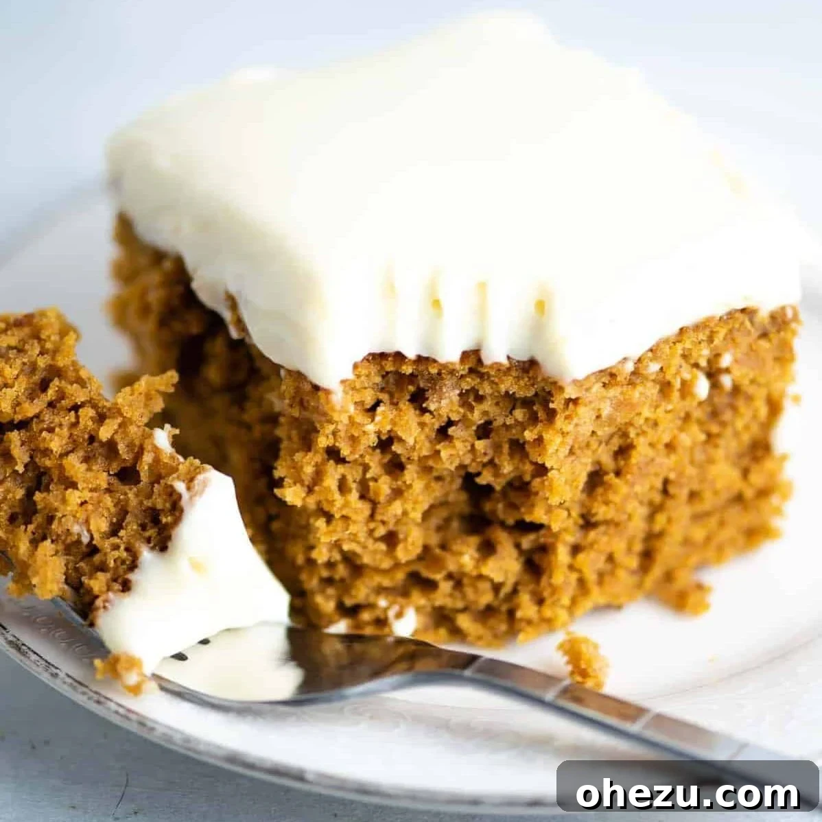 A slice of lightened up pumpkin cake with homemade cream cheese frosting on a white plate, with a bite taken out, highlighting its moist texture and creamy topping.