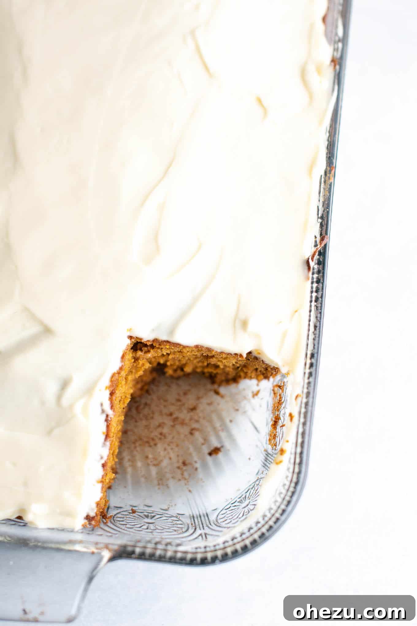 A 9x13 inch baking dish filled with a golden-brown pumpkin cake, with one slice carefully removed, revealing the soft interior and ready for frosting.