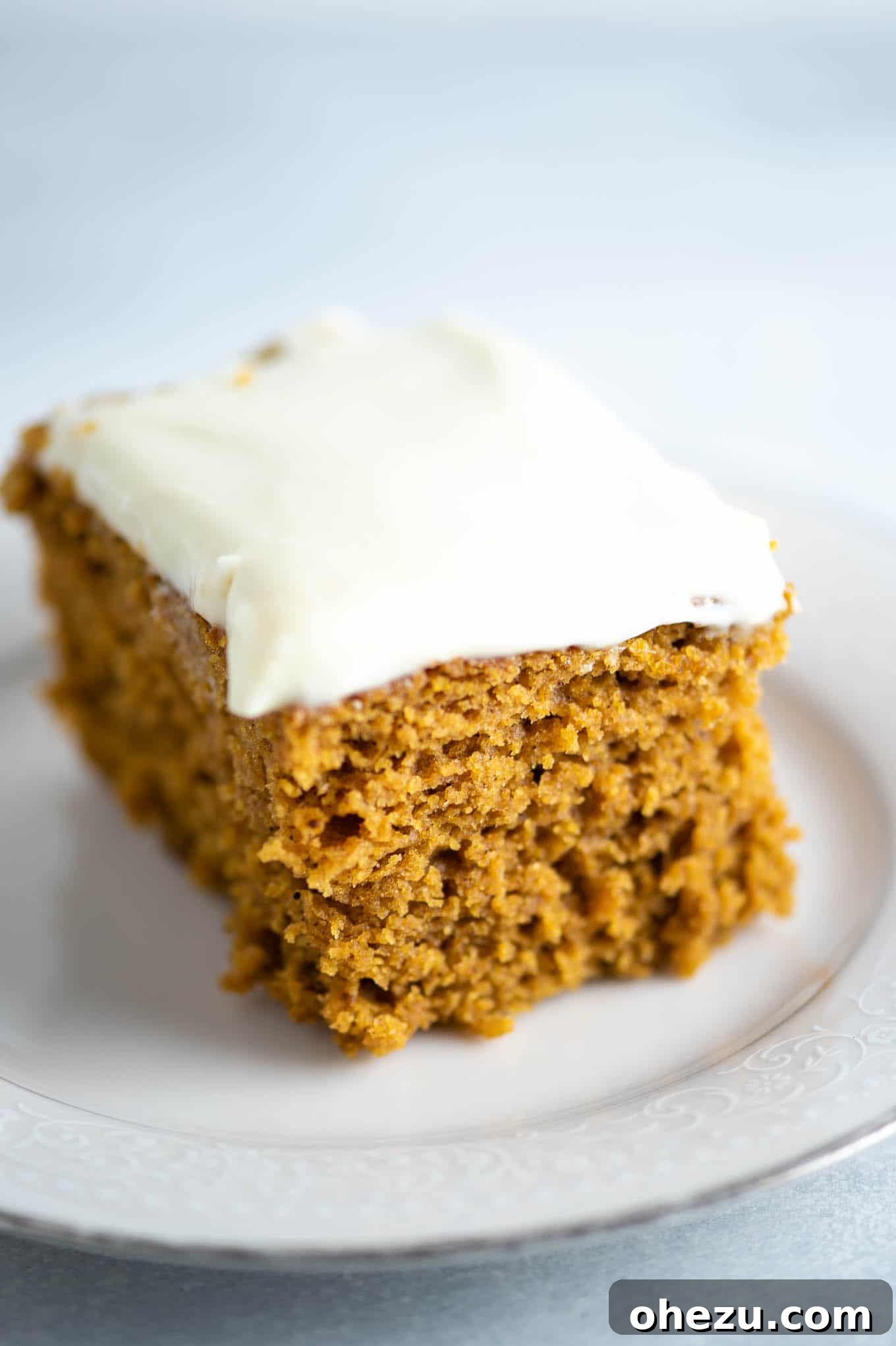 A perfectly sliced piece of lightened up pumpkin cake, generously topped with fluffy cream cheese frosting, ready to be enjoyed.