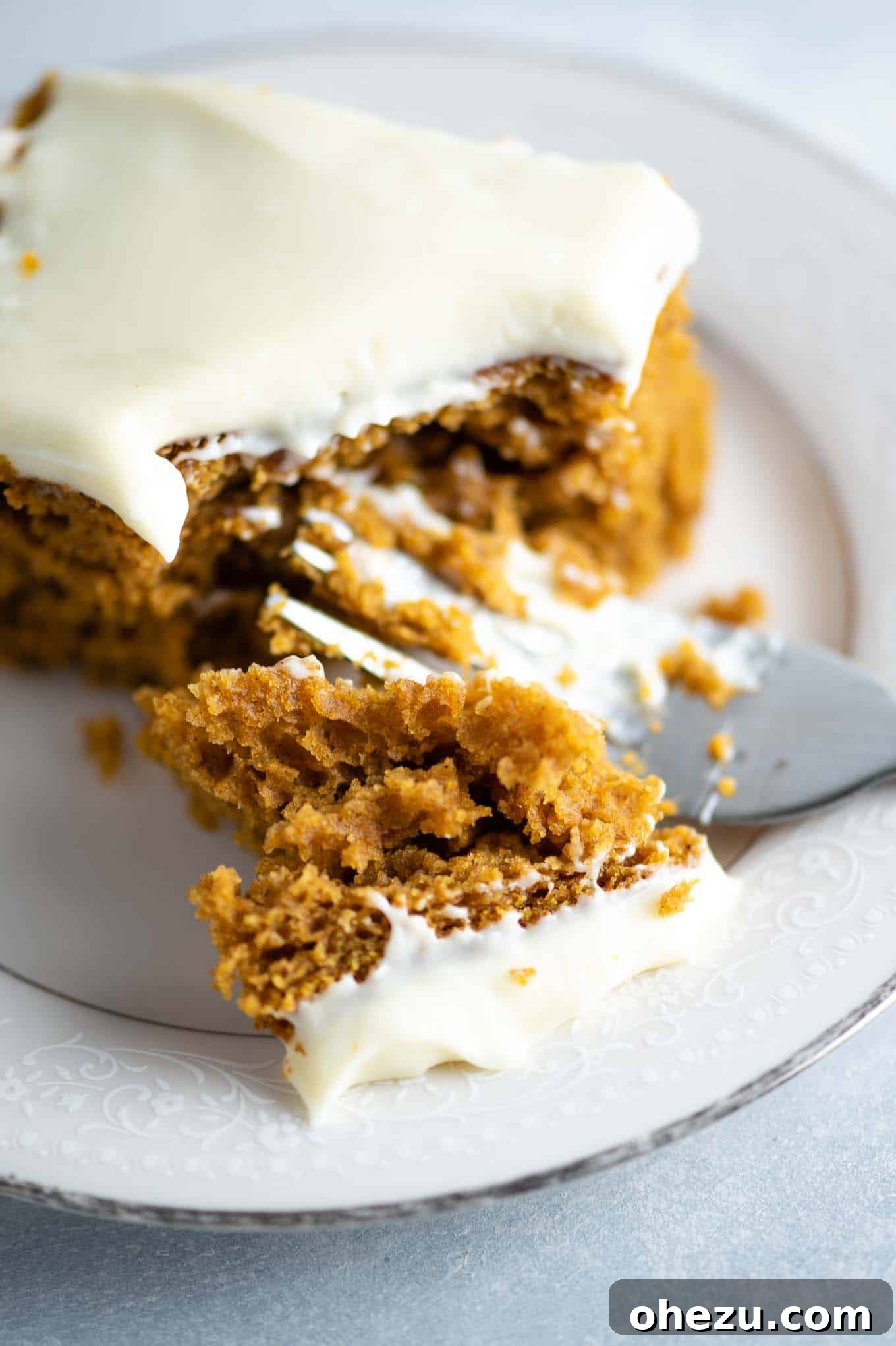 An inviting close-up of a bite of pumpkin cake with creamy frosting on a fork, ready to be eaten.