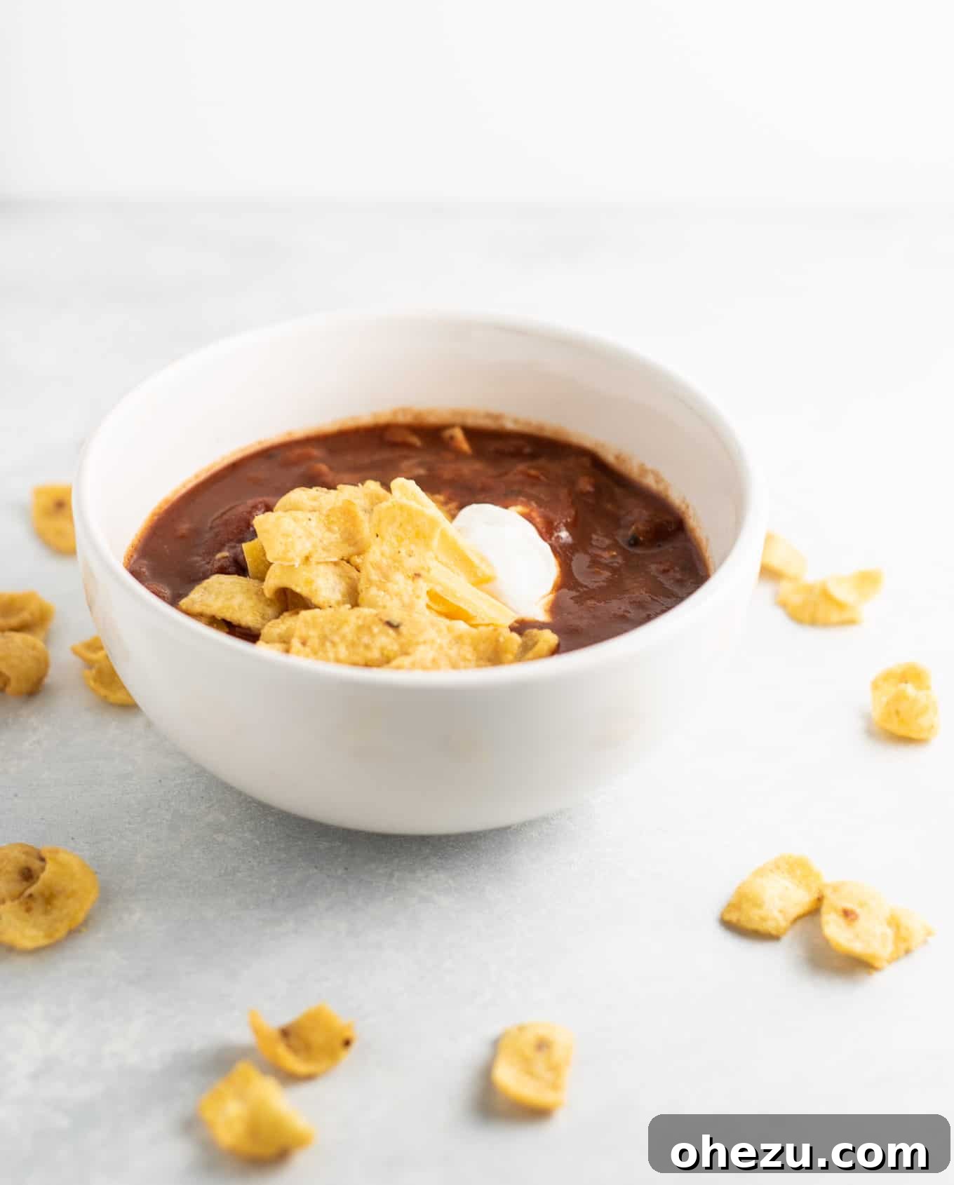 A bowl of rich chili generously topped with Fritos, sour cream, and shredded cheese, ready to be enjoyed.