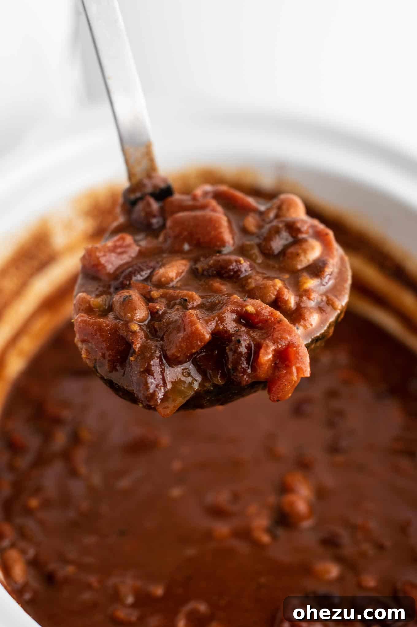 A ladle filled with hearty vegetarian chili, ready to be served.