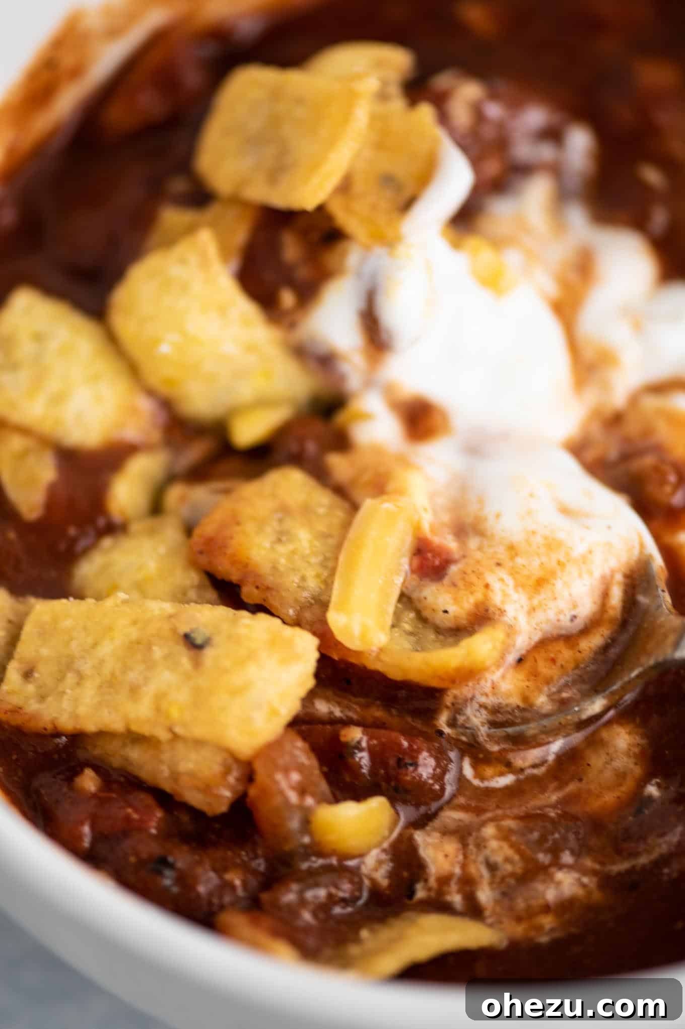 A close-up of vegetarian chili topped with a generous swirl of sour cream, shredded cheese, and crunchy corn chips.