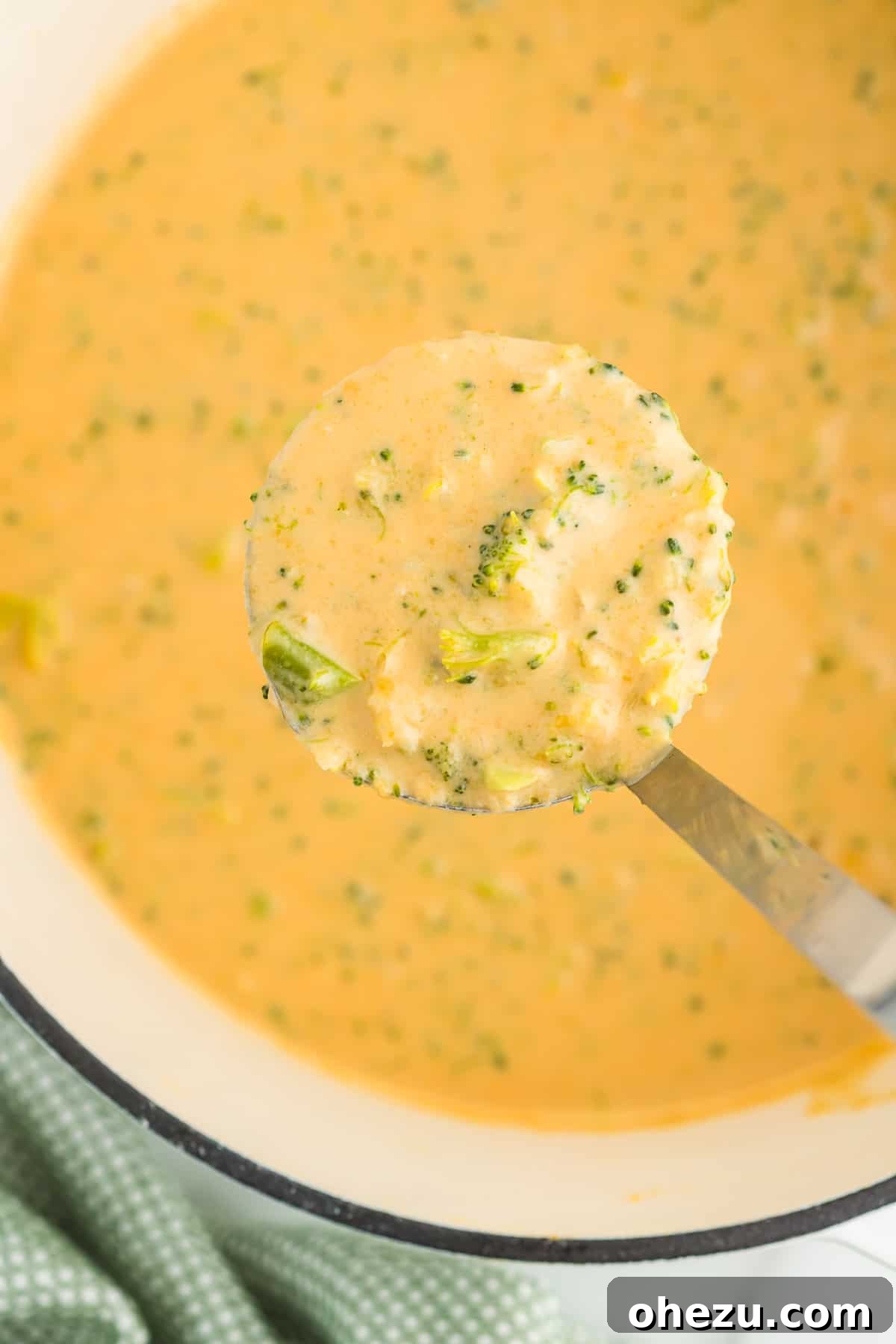 A ladle full of golden, creamy broccoli cheese soup, steaming hot and ready to be served into a bowl.