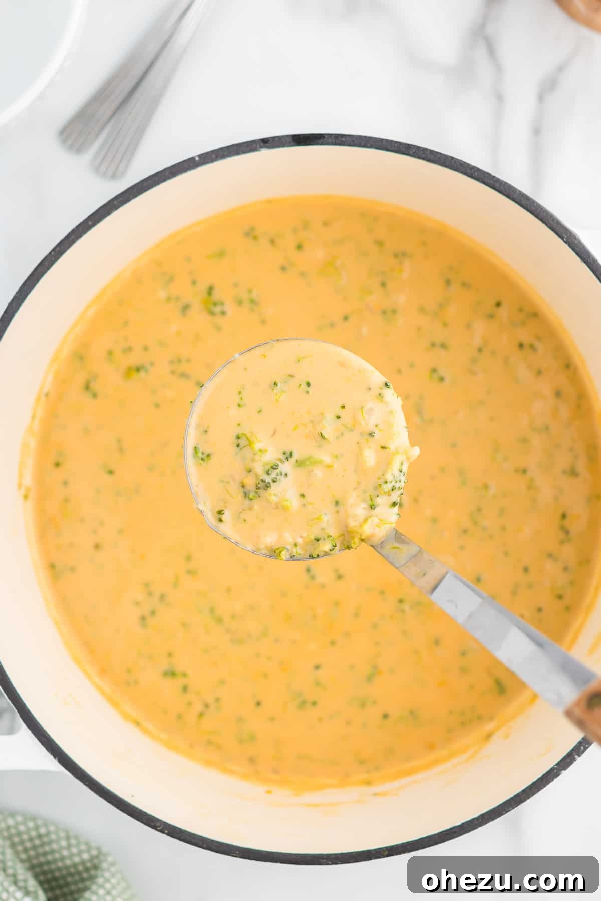 A steaming ladle of rich and creamy broccoli cheese soup, showing the perfectly melted cheese and tender small pieces of broccoli.