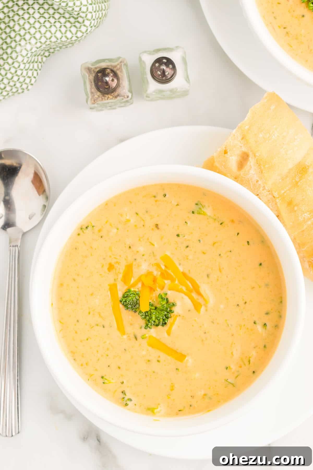 A large serving of creamy broccoli cheese soup in a white bowl with a spoon, showing its inviting texture and warmth.