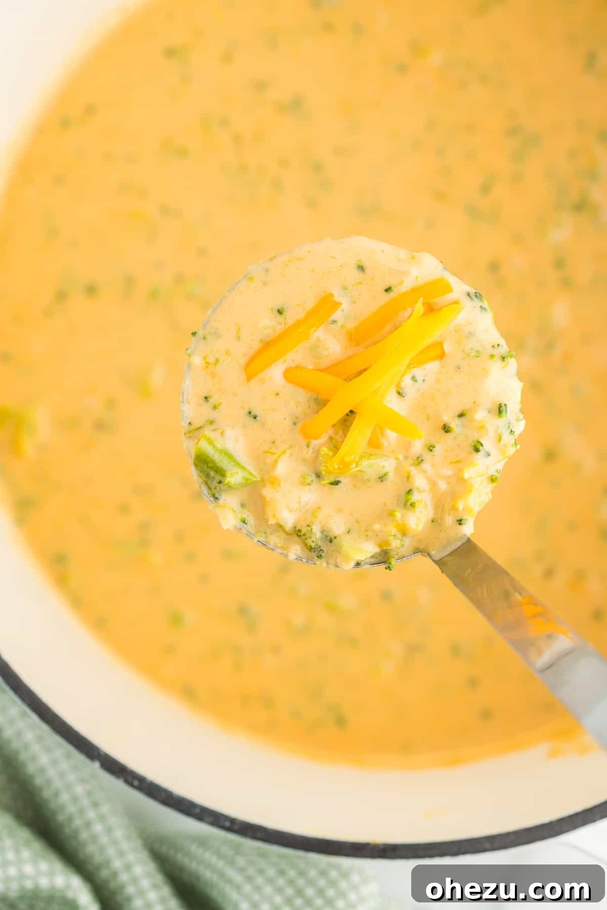 A final close-up of a generous serving of creamy broccoli cheese soup in a white bowl, with steam gently rising, inviting you to take a spoonful.
