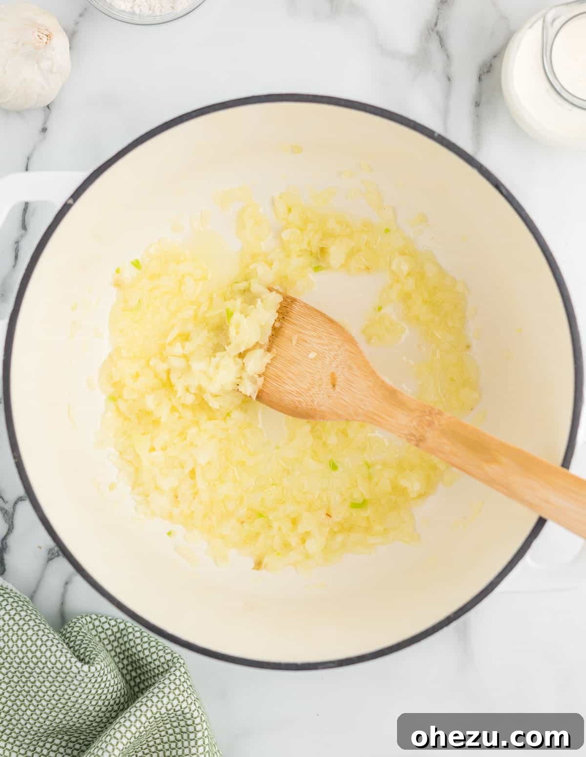 Finely diced yellow onions cooking in melted butter in a heavy-bottomed Dutch oven on a stovetop, softening gradually.