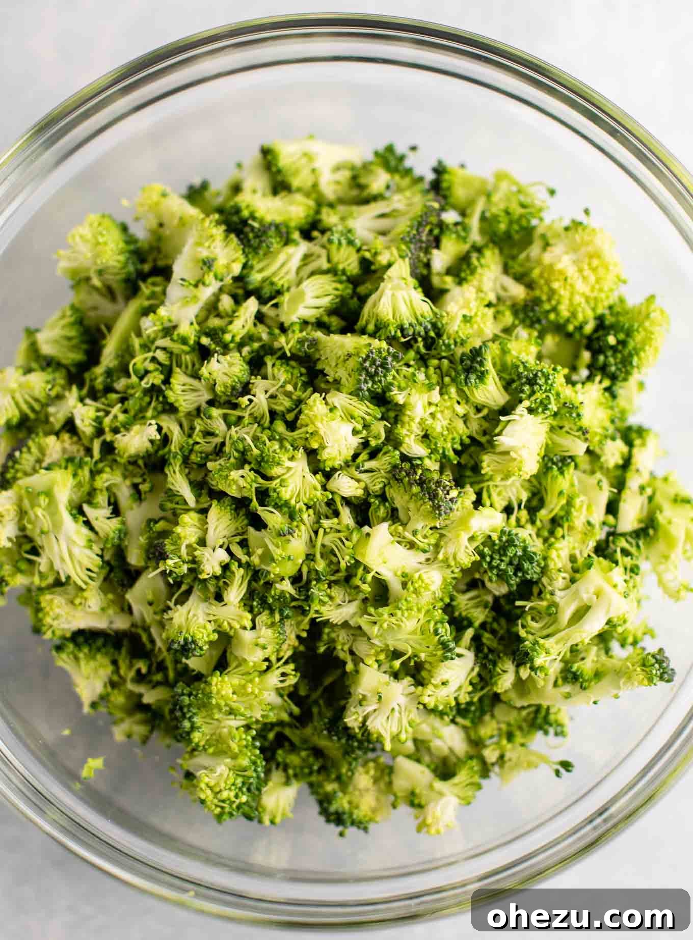 A transparent bowl filled with fresh, vibrant green, finely chopped broccoli florets, perfectly prepared and ready to be added to the soup.