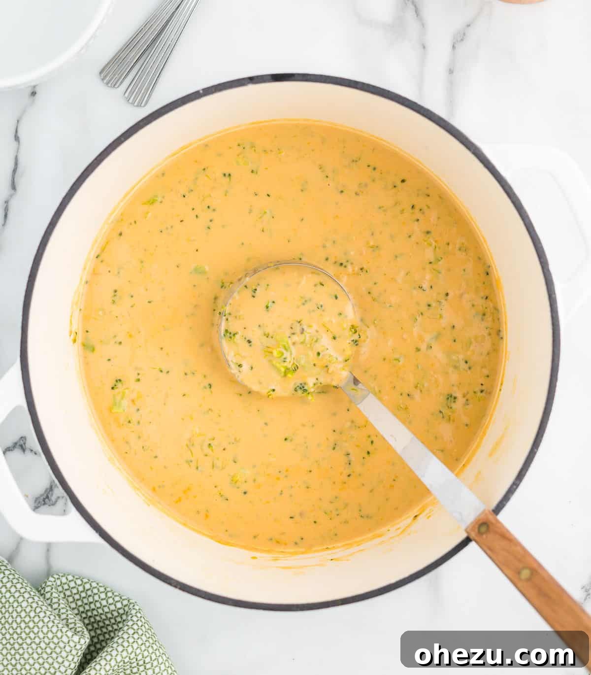 A close-up shot of creamy broccoli cheese soup being stirred with a wooden ladle in a Dutch oven, showing the melted cheese and tender broccoli pieces.
