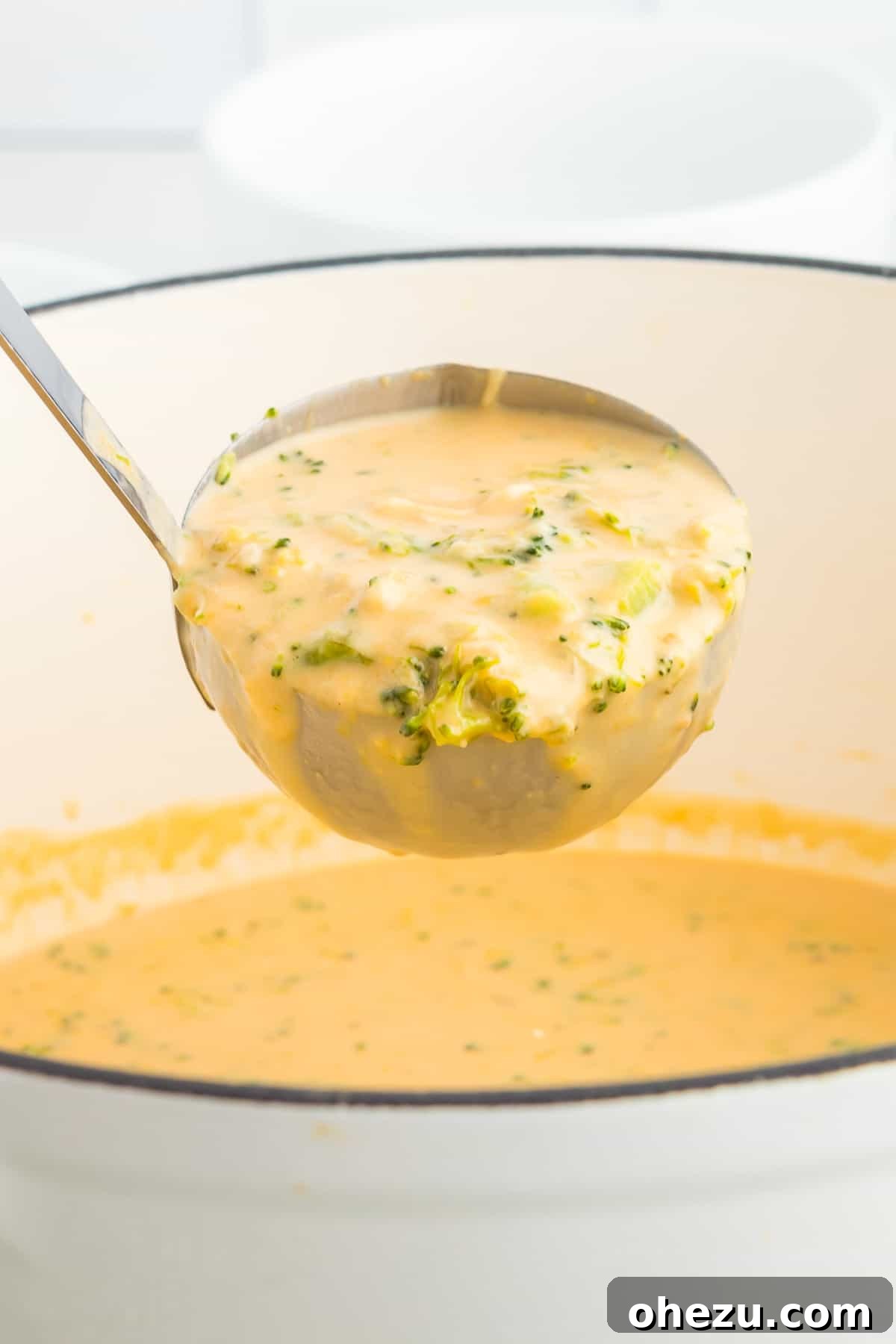 A full ladle brimming with rich and creamy broccoli cheese soup, glistening and ready to be served from the pot into a bowl.