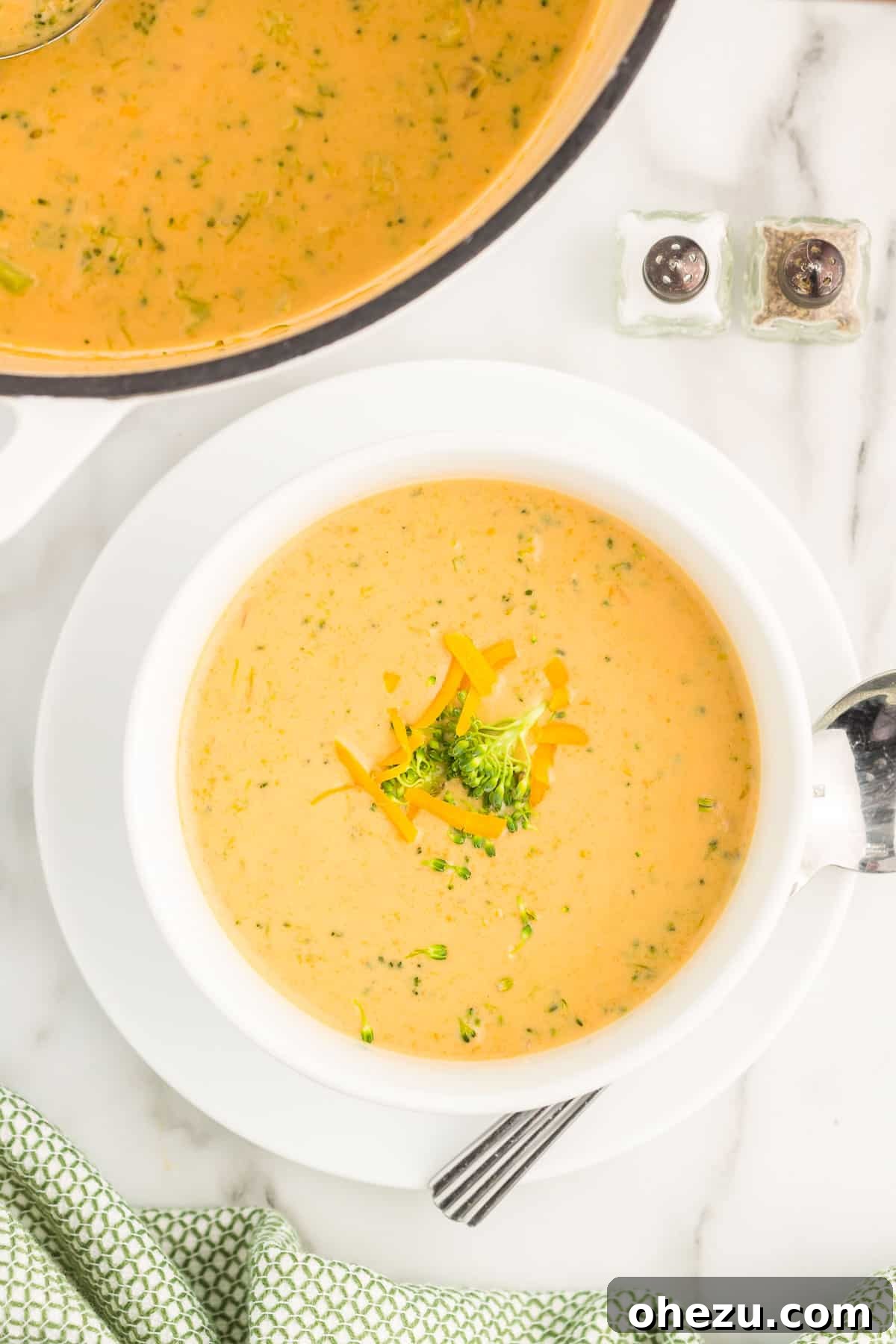 A generous serving of creamy broccoli cheese soup in a classic white ceramic bowl, accompanied by a spoon, resembling a cafe-style presentation.