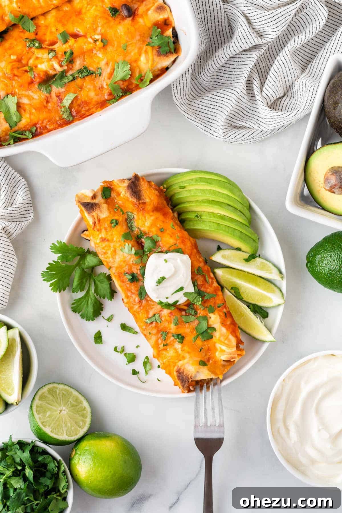 Delicious vegetarian enchiladas on a plate, garnished with sour cream, fresh lime, and avocado slices.