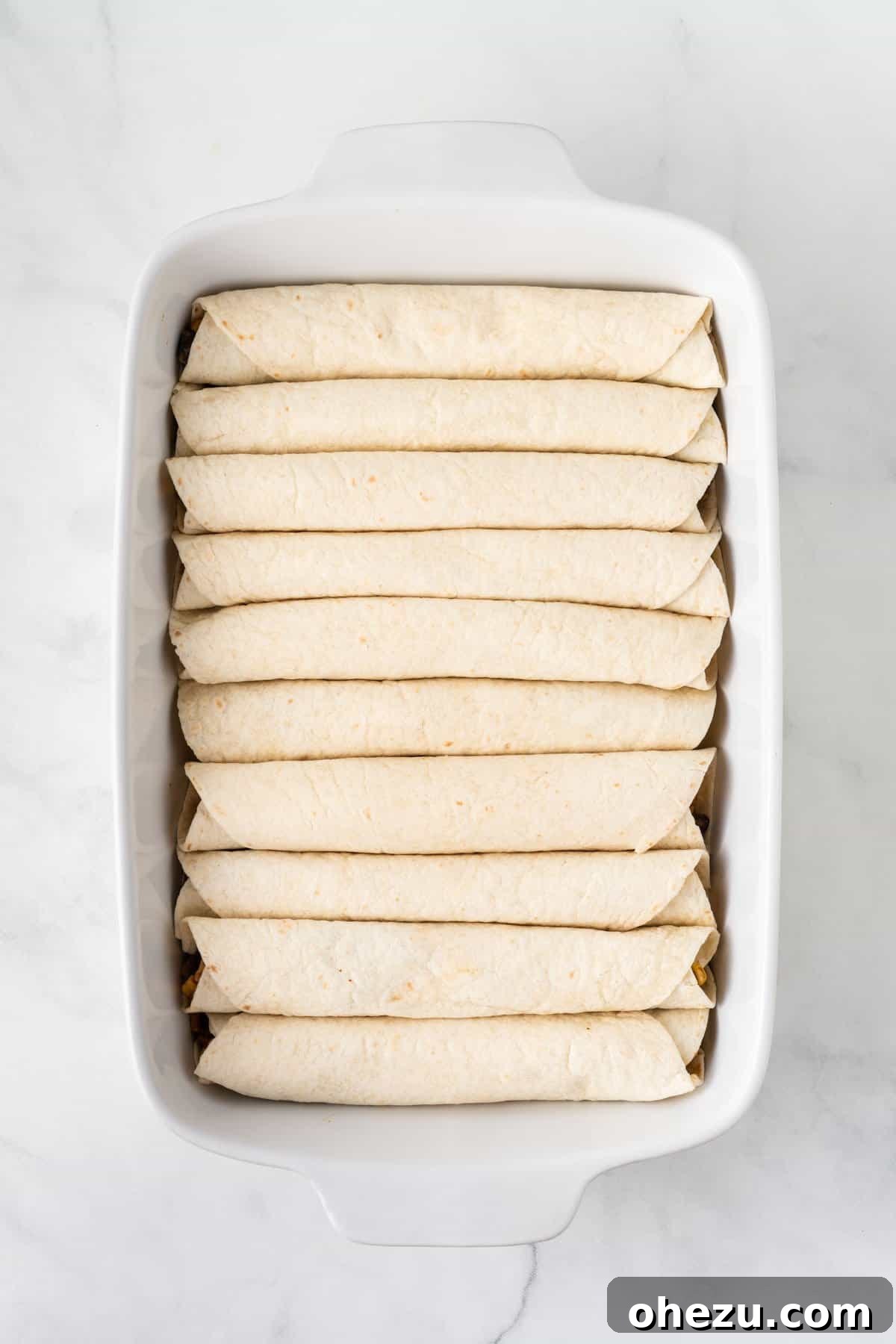 A large 9x13 baking dish neatly filled with rolled-up vegetarian enchiladas, arranged seam-side down, ready for sauce.