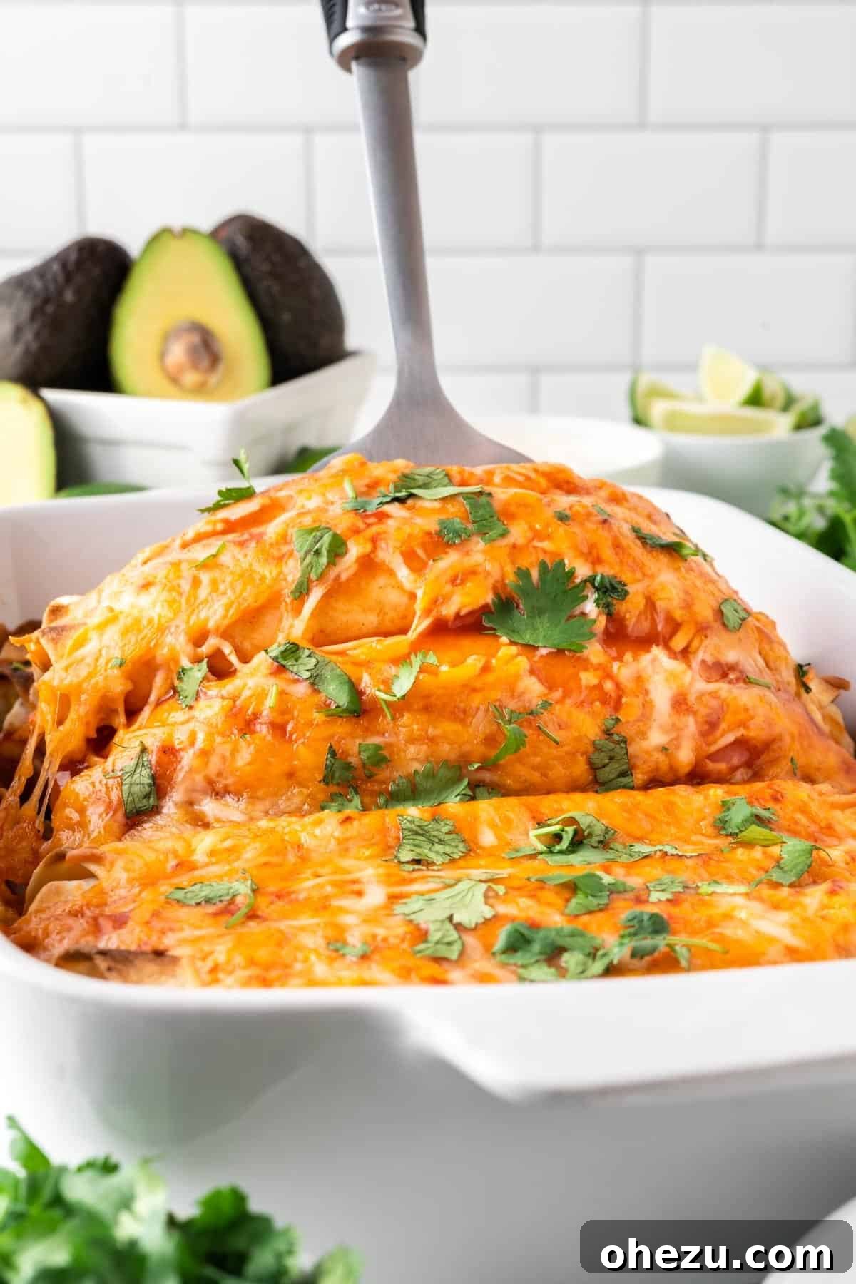 Scooping a generous portion of cheesy vegetarian enchiladas directly from the baking pan onto a serving plate, steaming hot.