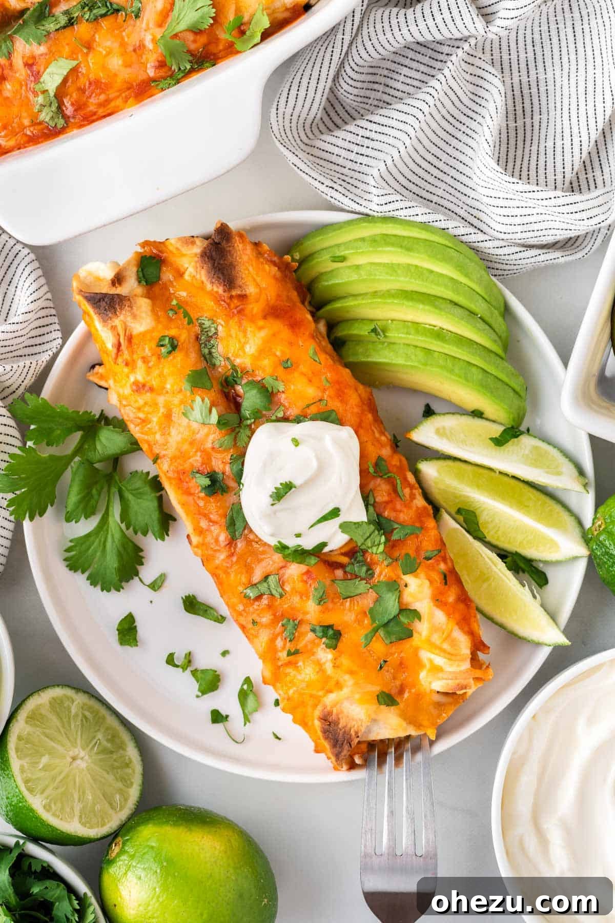 A close-up shot of a perfect serving of vegetarian enchiladas on a plate, topped with sour cream and garnished with fresh lime and avocado slices.
