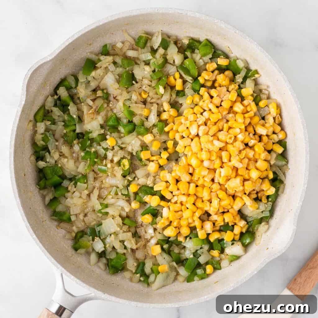 Adding frozen corn kernels to the mixture of sautéed vegetables in the skillet for further cooking.