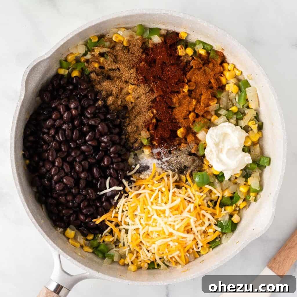 Black beans, cream cheese, Mexican cheese, and spices being added to the cooked vegetables in a skillet for the filling.