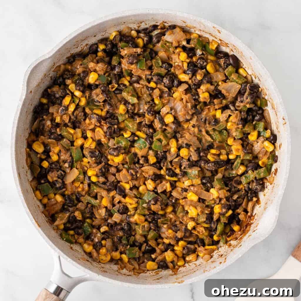 The creamy enchilada filling, rich with vegetables, beans, and melted cheese, stirred together and ready in a skillet.