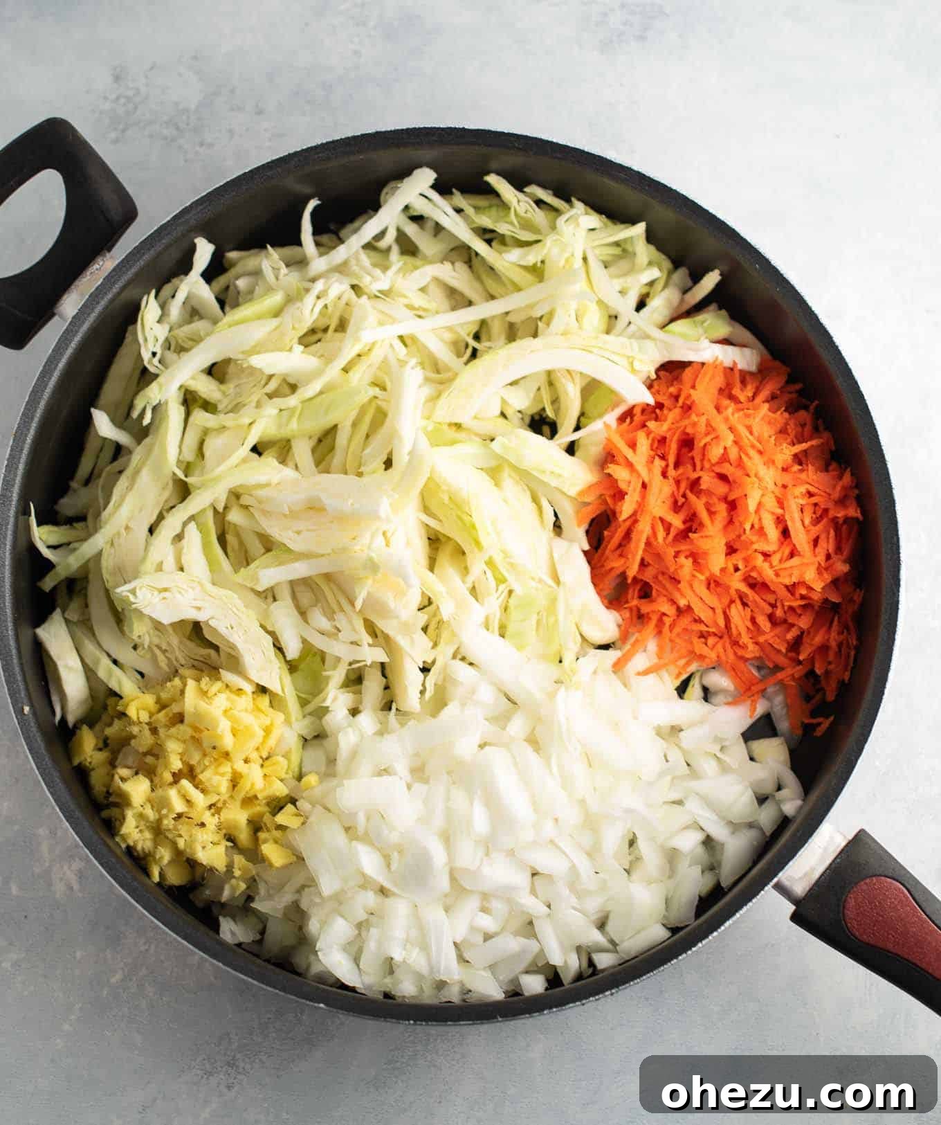 A large skillet filled with raw ginger, diced onion, fresh cabbage, and grated carrots, glistening with sesame oil.
