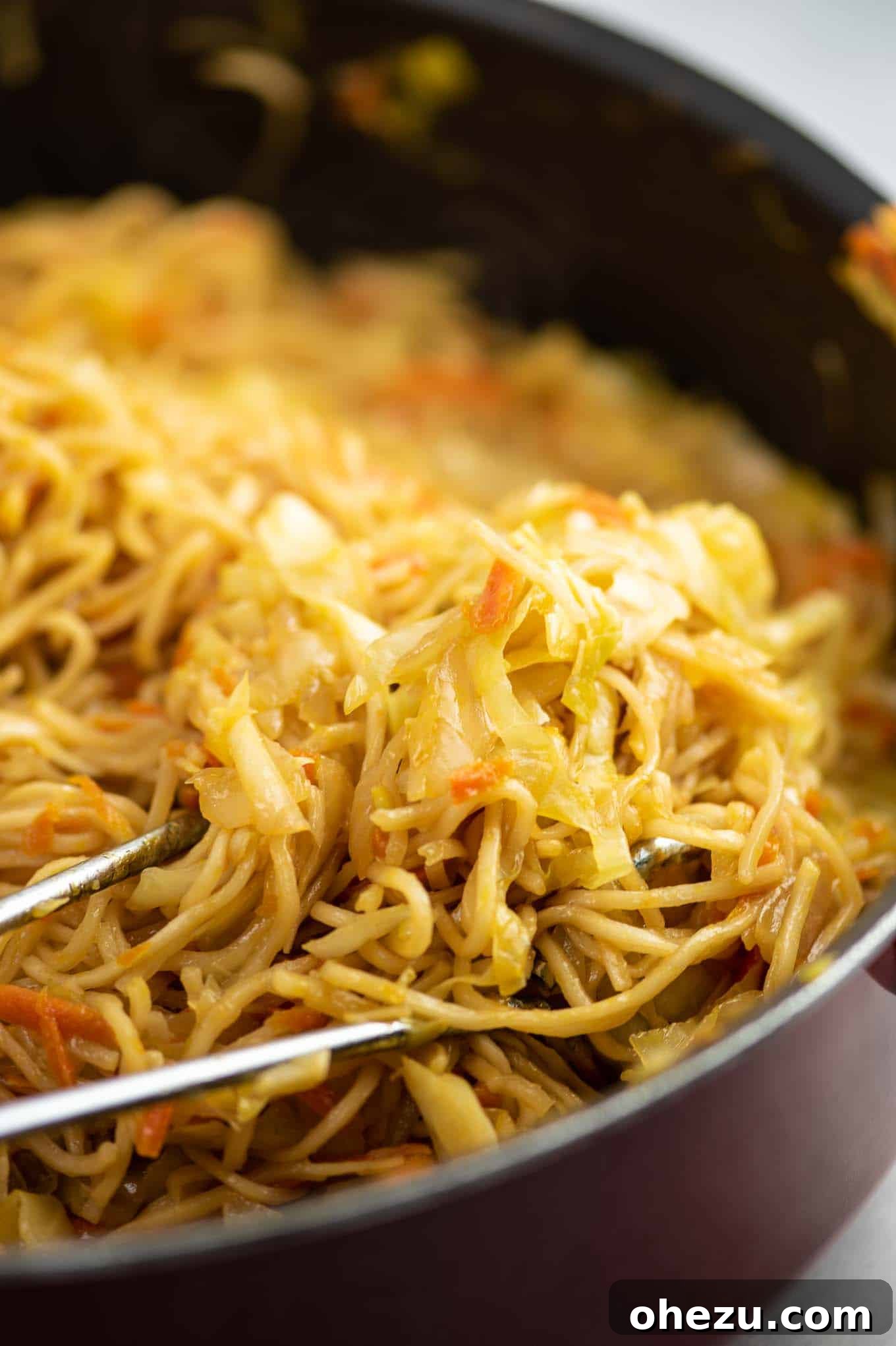 The cabbage stir fry in a skillet, being tossed with tongs to ensure even cooking and distribution of ingredients.