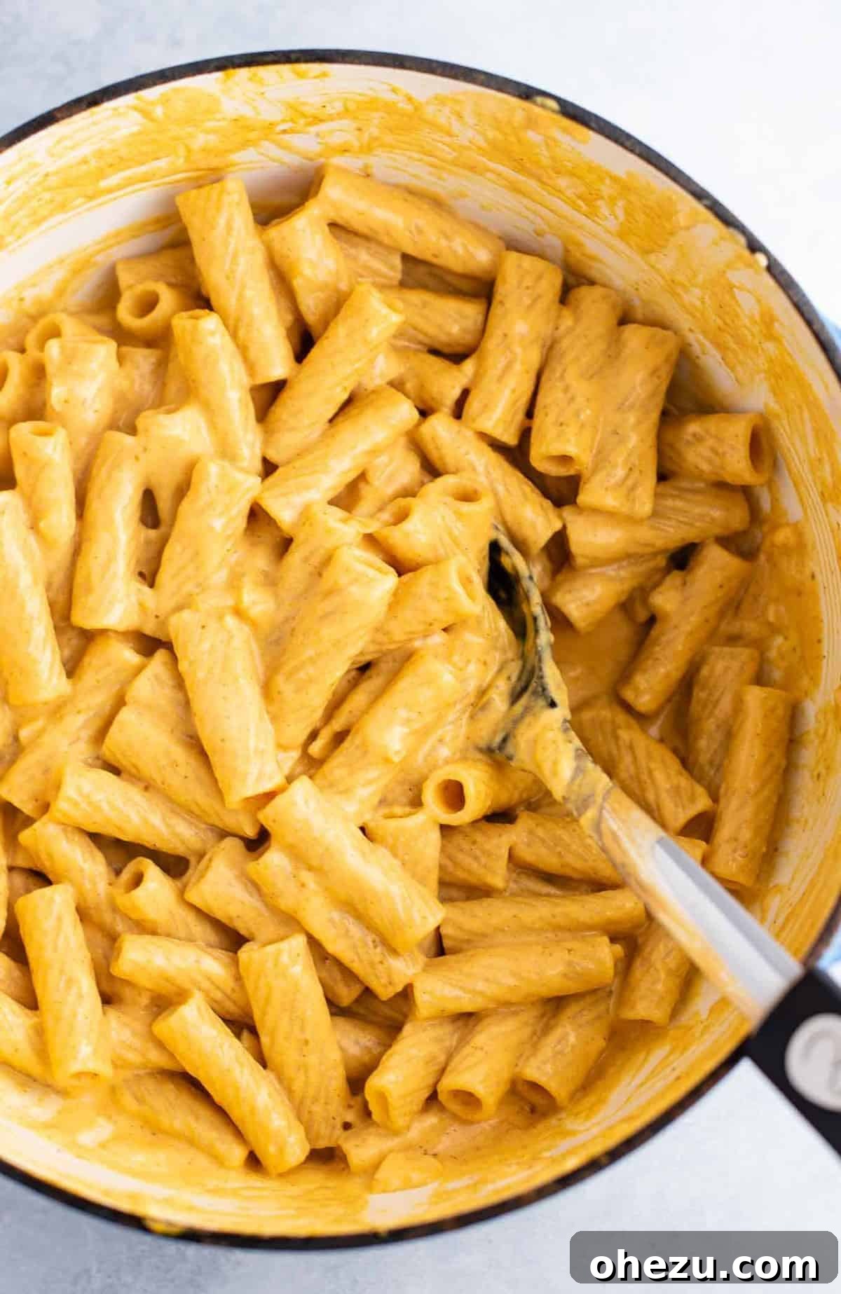 rigatoni mixed with pumpkin pasta sauce with a spoon in the dish