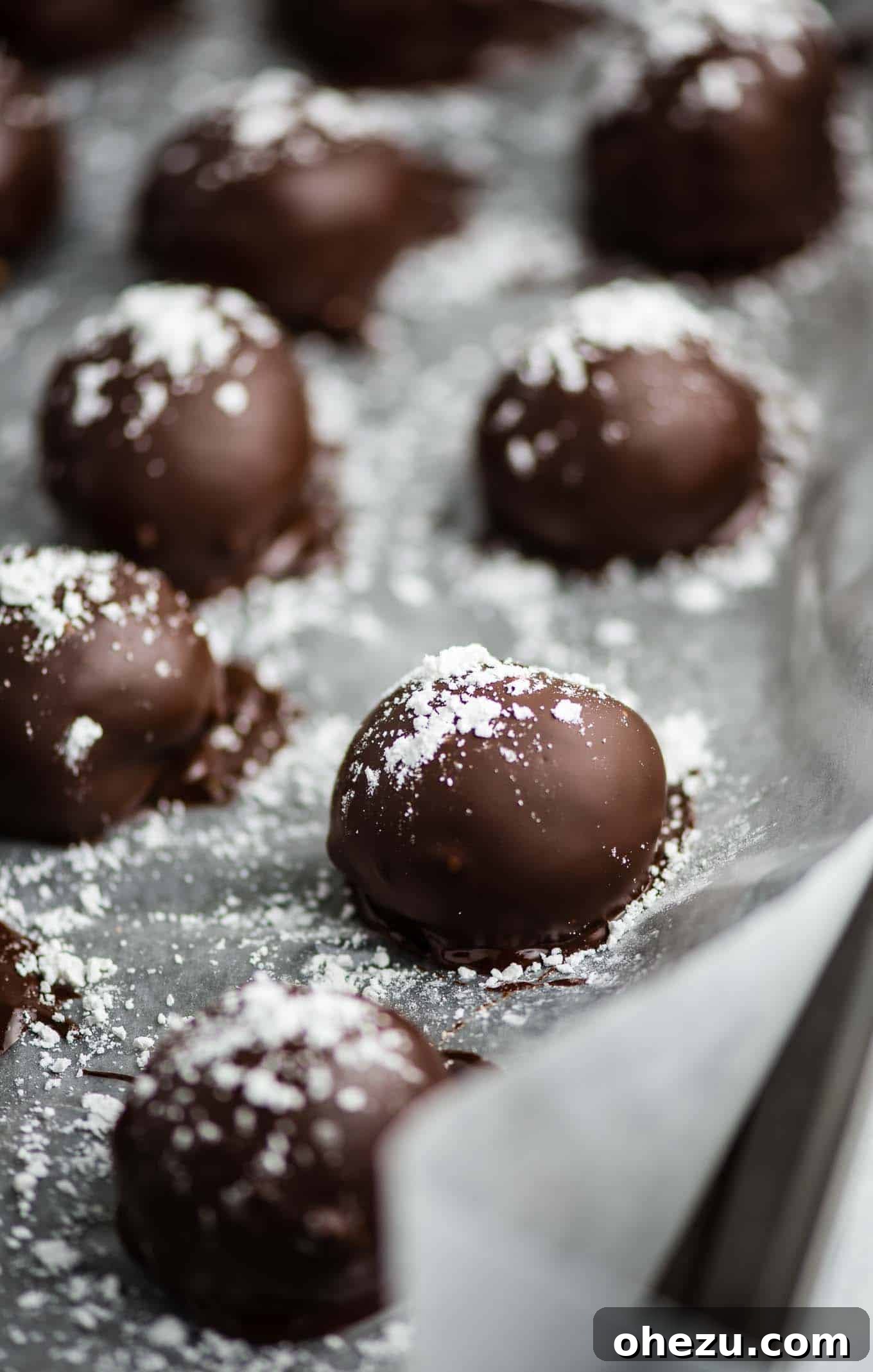 Pumpkin truffles lined up on a baking sheet, freshly sprinkled with powdered sugar