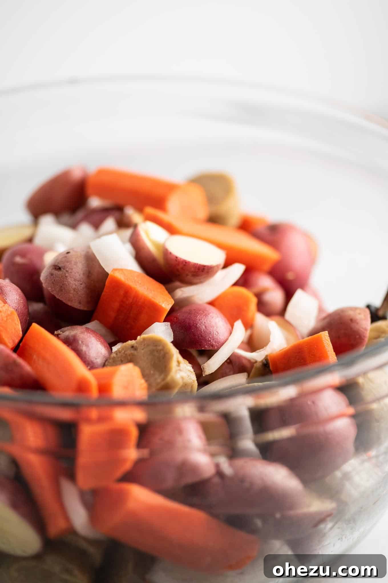 Sliced baby red potatoes, carrots, onions, and vegetarian kielbasa expertly chopped and mixed in a large bowl, ready for seasoning.