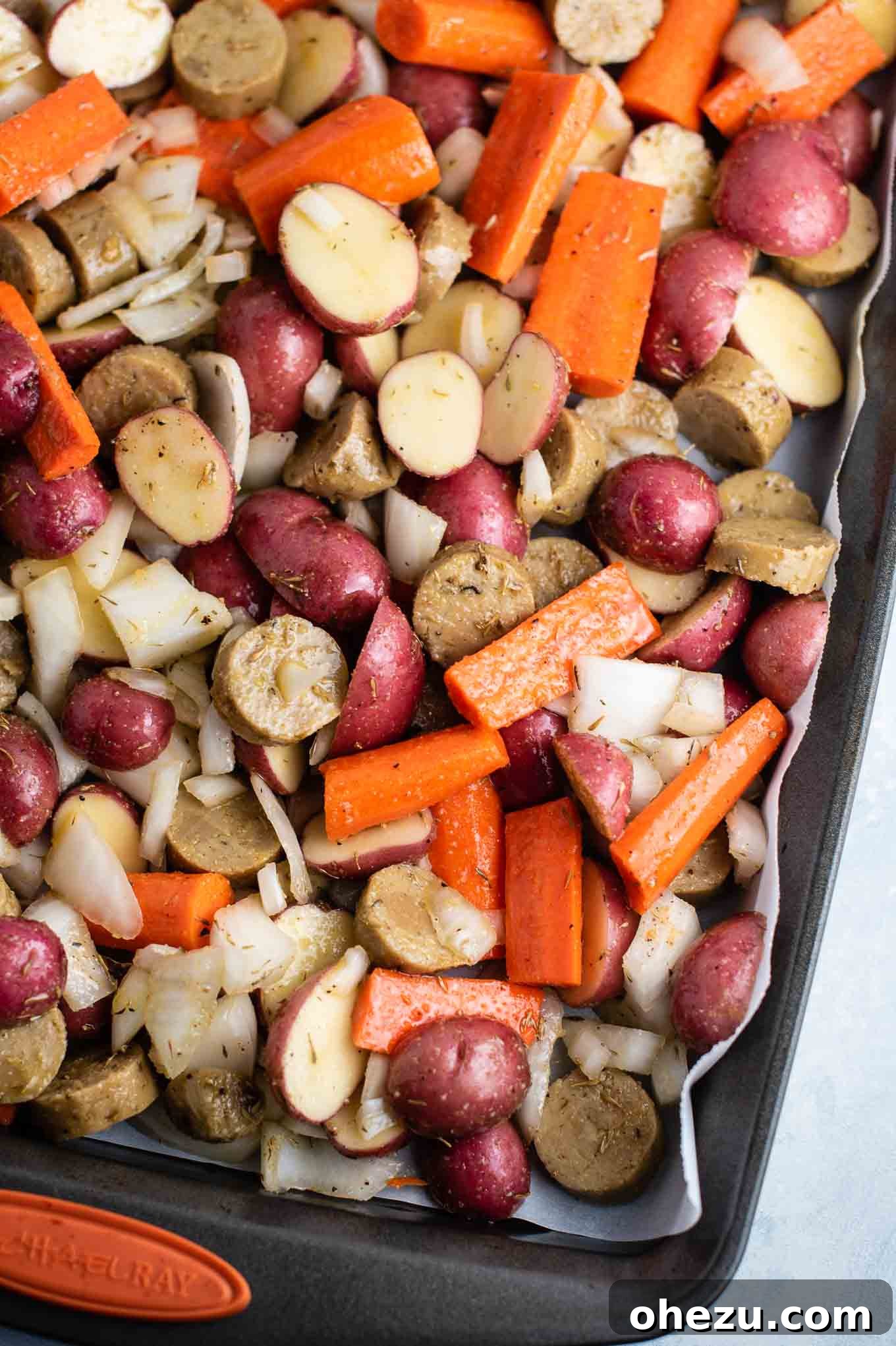 Sheet pan with vegetarian kielbasa and all vegetables mixed with spices and olive oil, arranged in an even layer prior to baking.