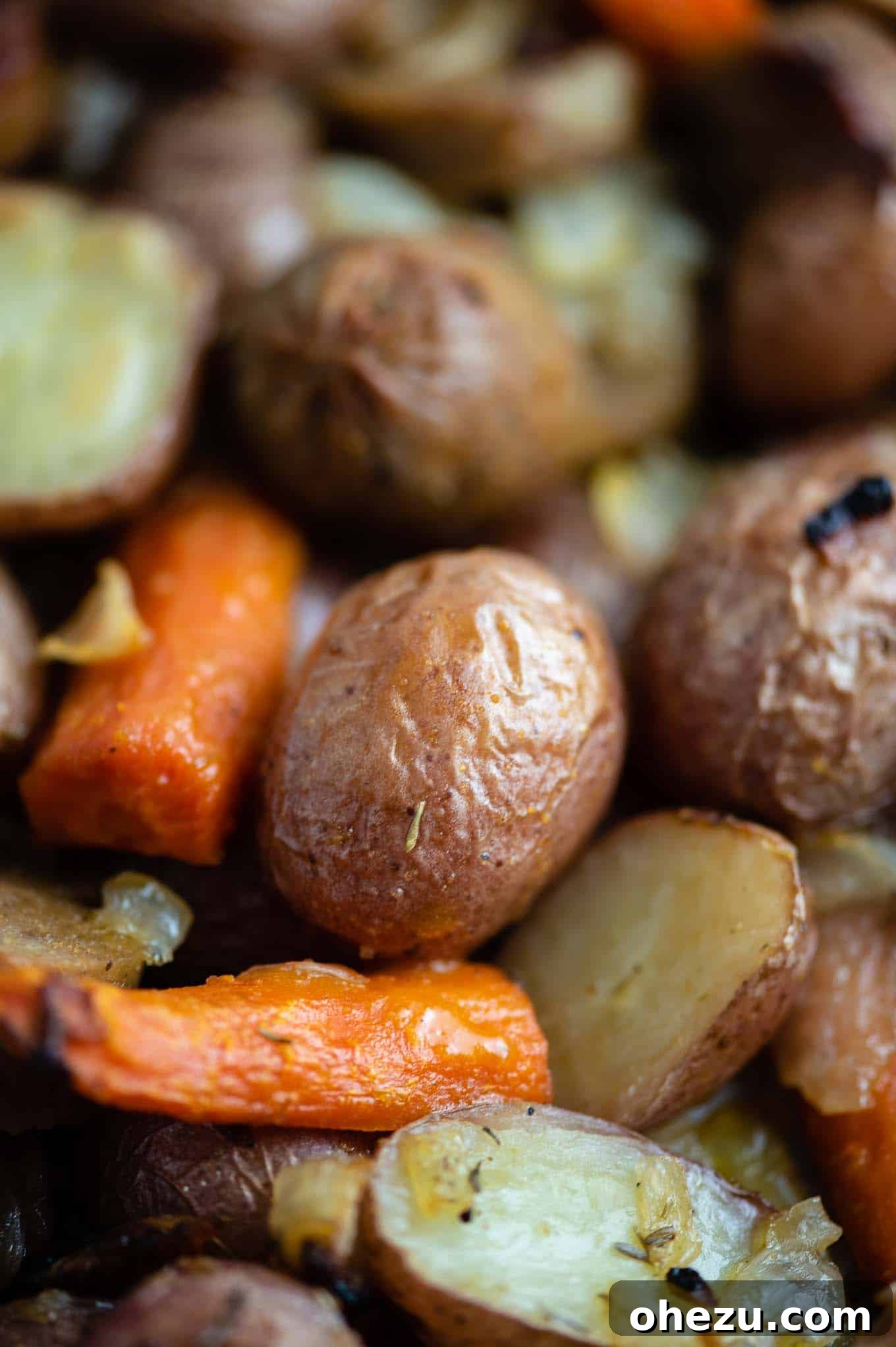 Close-up shot of roasted potatoes and carrots with golden-brown, crispy edges on a sheet pan.