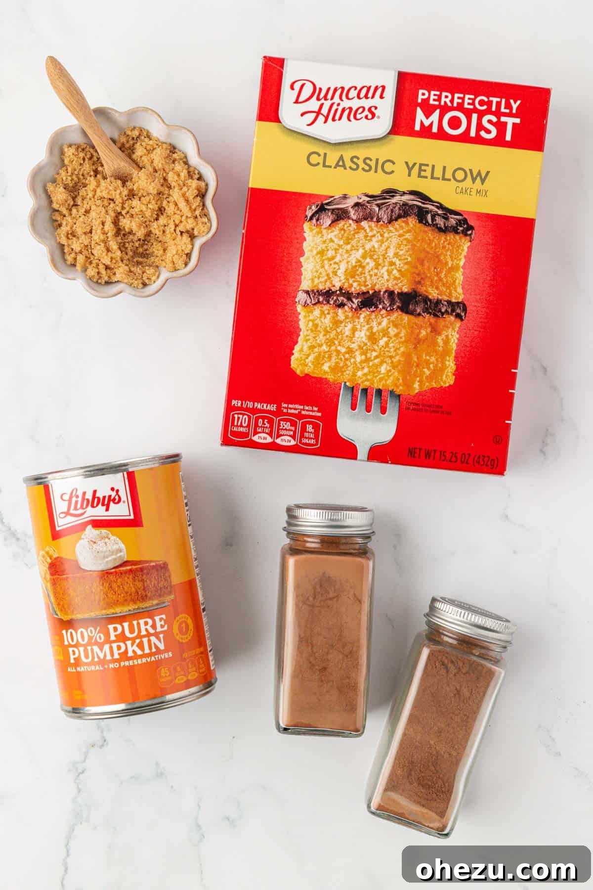 A collection of the 4 essential ingredients laid out: yellow cake mix box, canned pumpkin, pumpkin pie spice, and cinnamon, ready to make easy pumpkin muffins