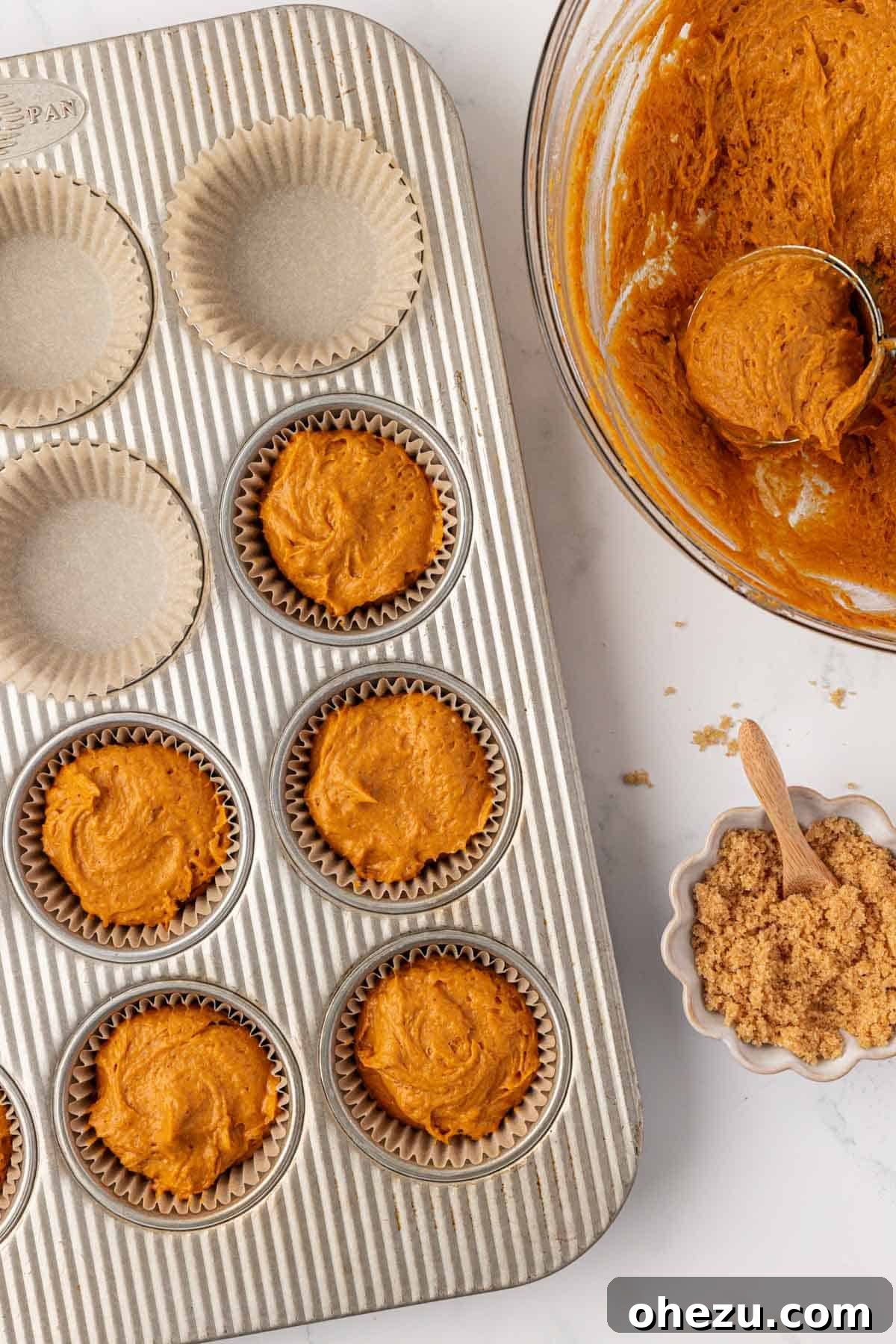 Pumpkin muffin batter carefully scooped into parchment-lined muffin cups