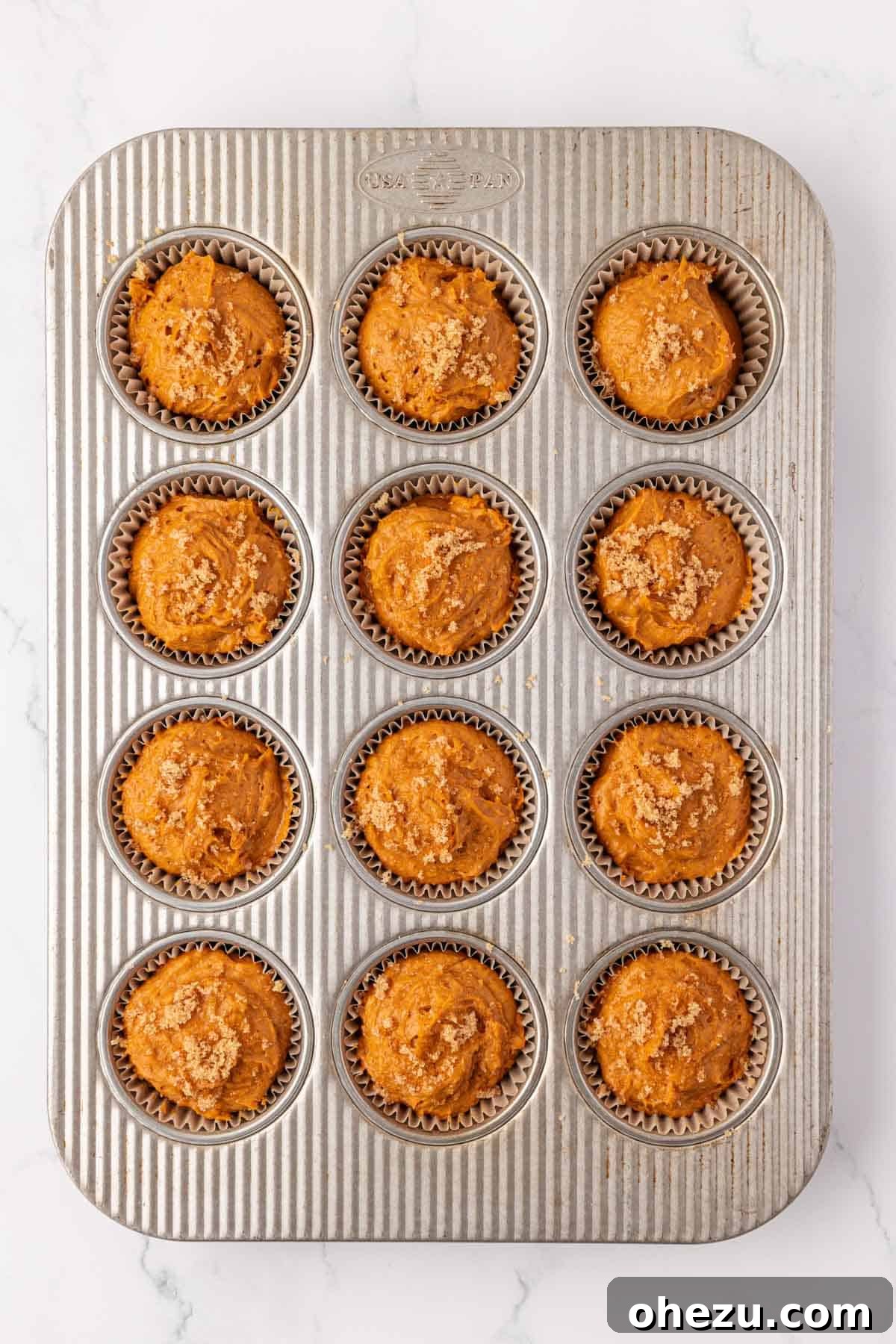 Muffin tin filled with pumpkin batter and brown sugar topping, ready to bake