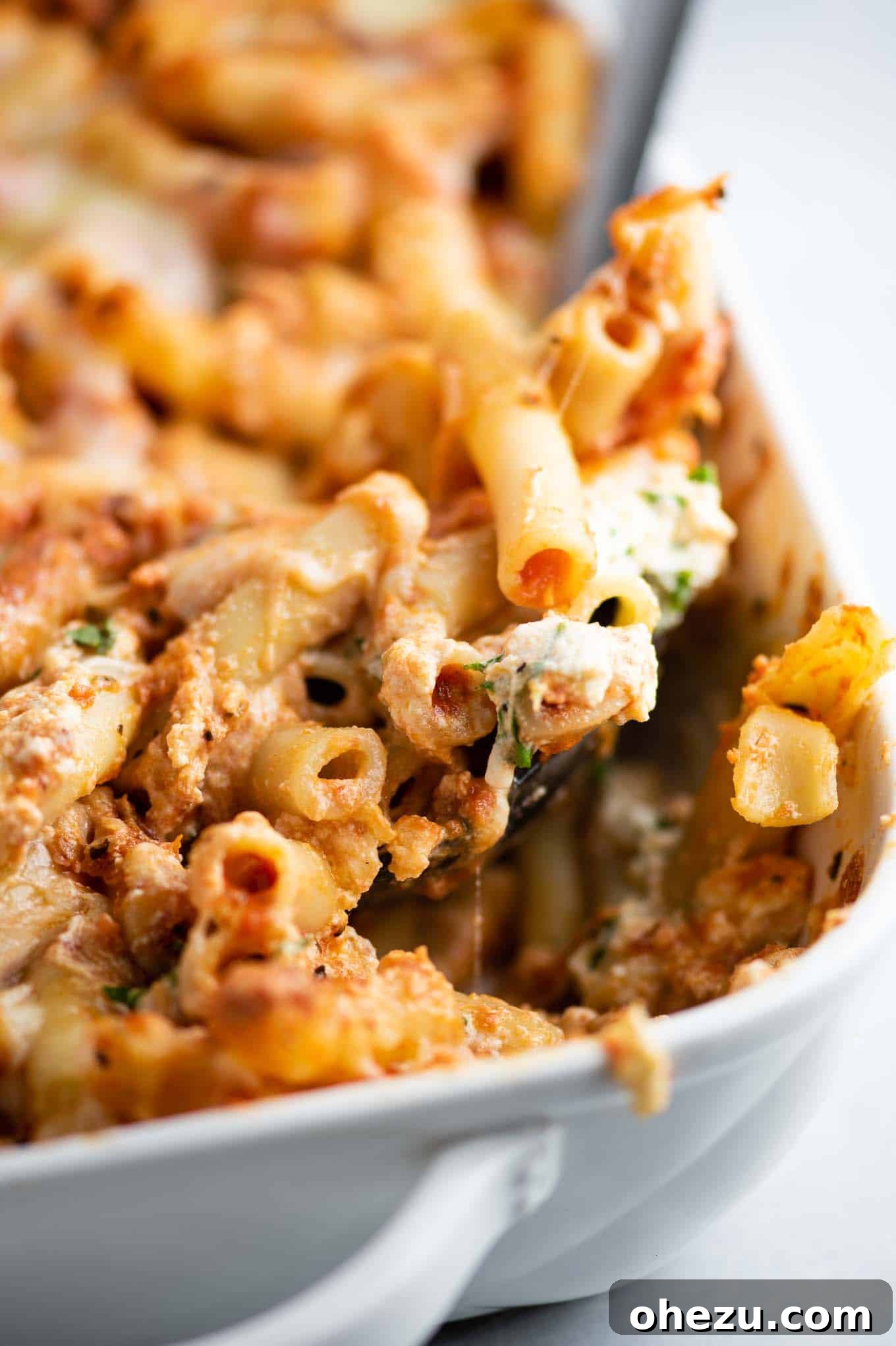 a spoon dishing out a scoop of ziti from the pan, showing layers of cheese and sauce
