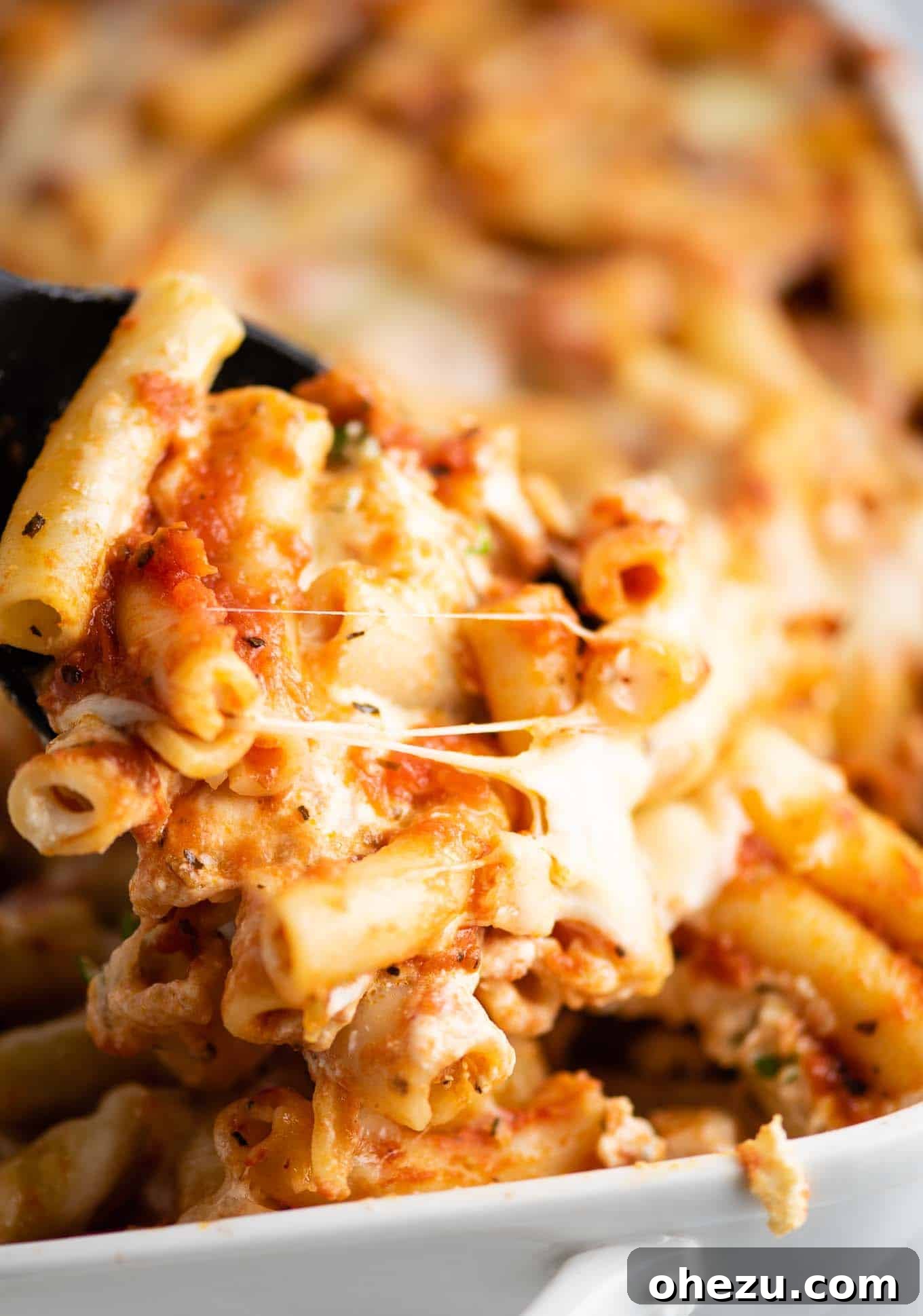 scoop of baked ziti coming out of the dish, showing hot, melted cheese