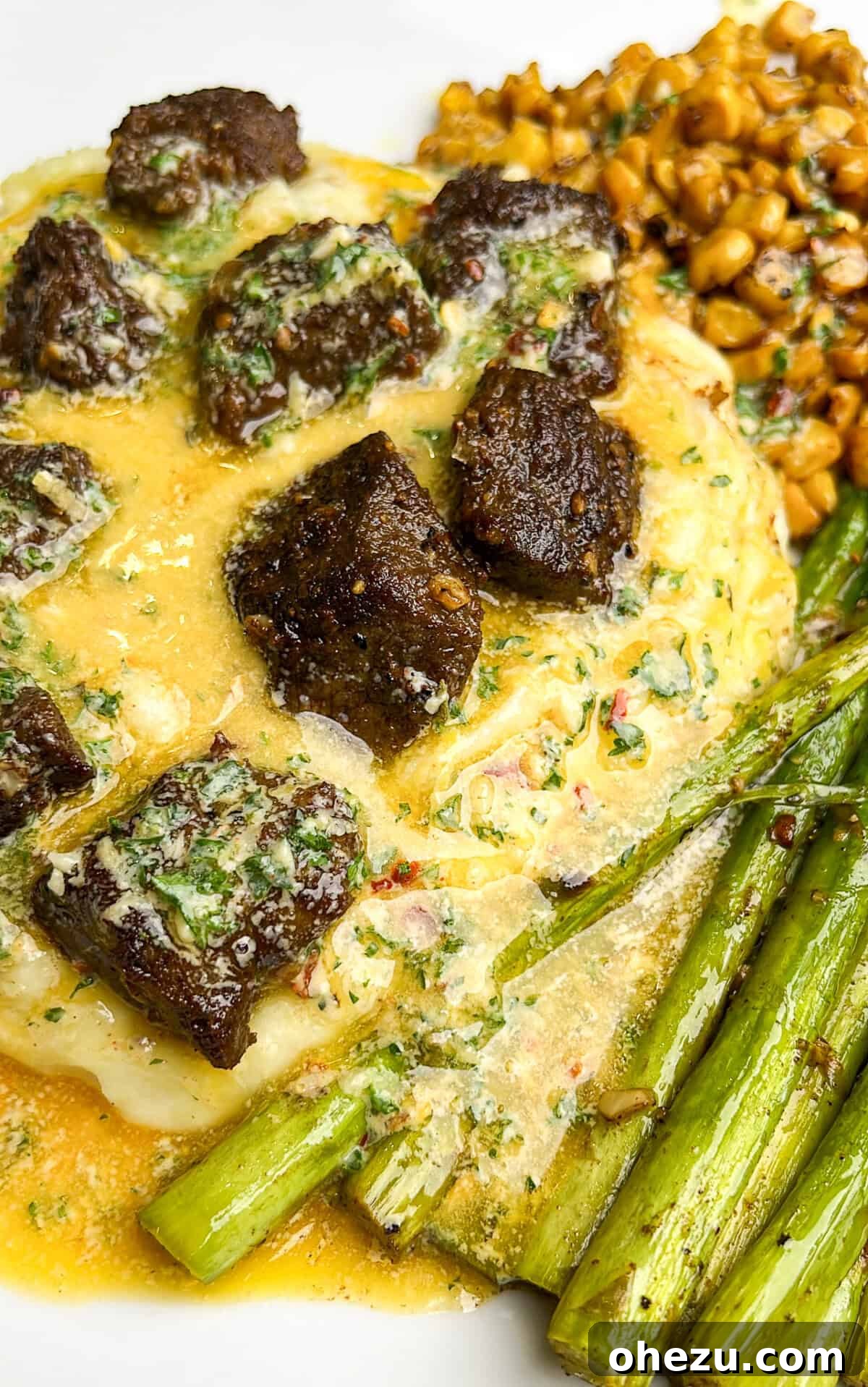 Dinner plate with golden brown steak bites, creamy mashed potatoes, bright green asparagus, and sweet corn, all generously drizzled with golden cowboy butter.