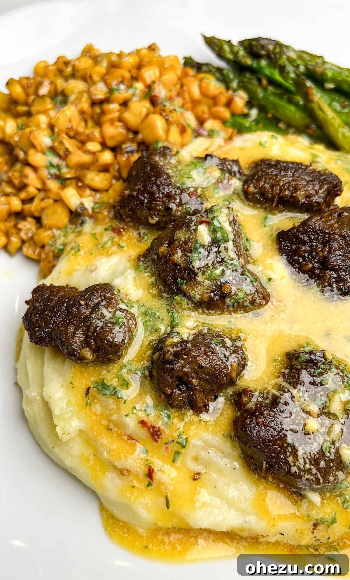 A beautifully presented dinner plate featuring steak, potatoes, asparagus, and corn, generously drizzled with cowboy butter, ready for a delicious meal.