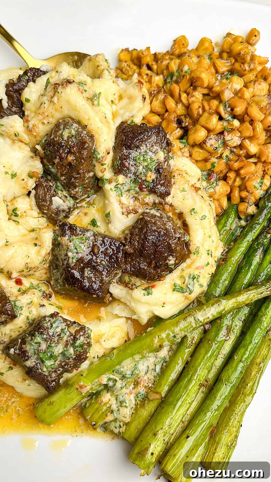 Close-up view of a dinner plate showcasing the texture of the steak, potatoes, asparagus, and corn glistening with cowboy butter.