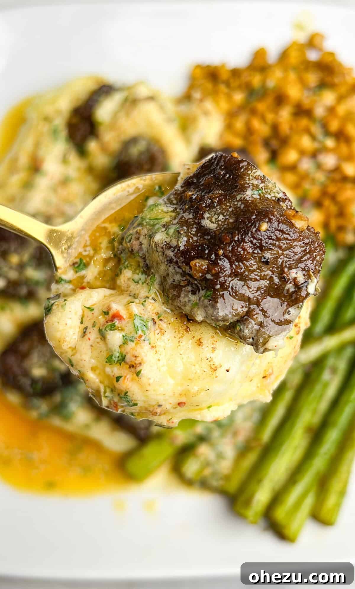 A serving spoon lifting a portion of steak and potatoes from a larger dish, showing the rich texture and juices.