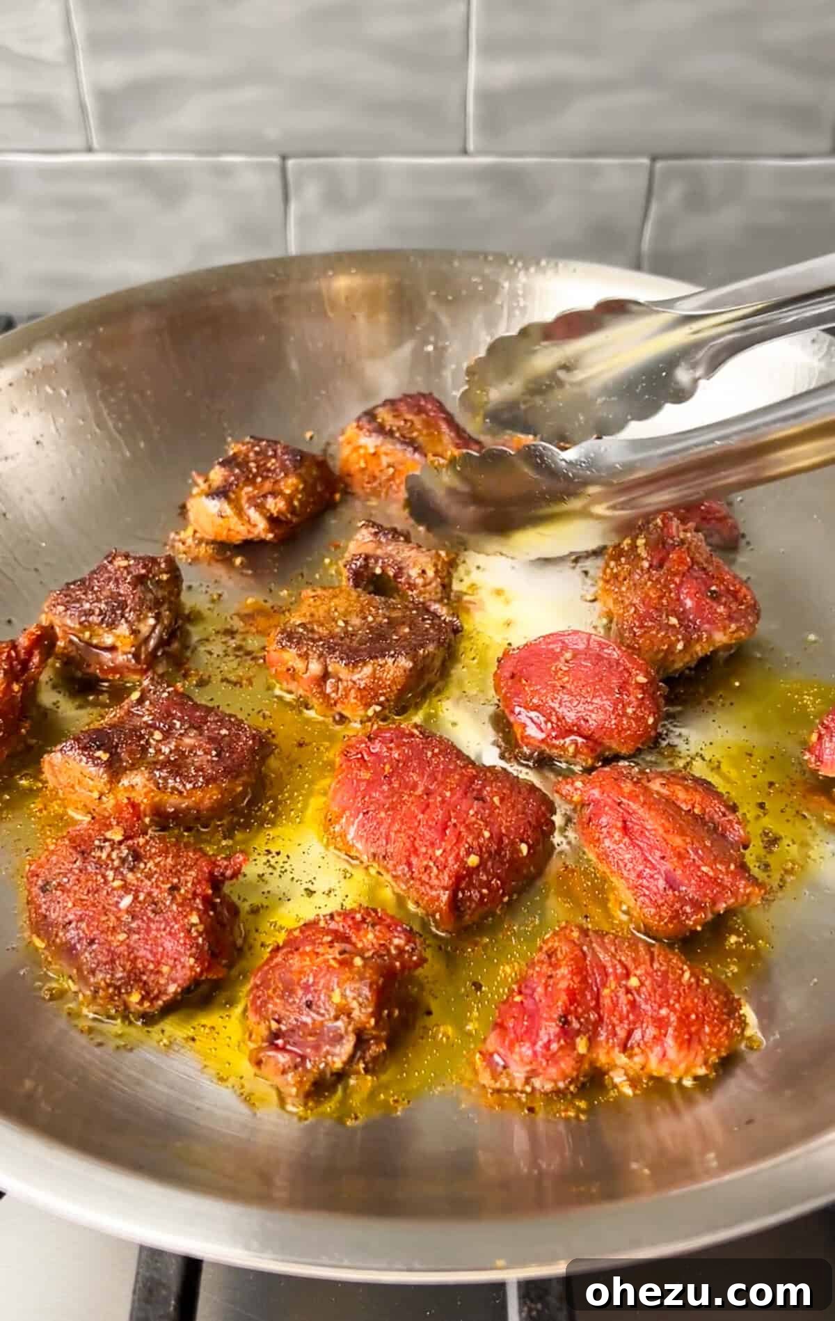 Steak bites searing in a hot skillet with avocado oil, showing a nice crust forming.