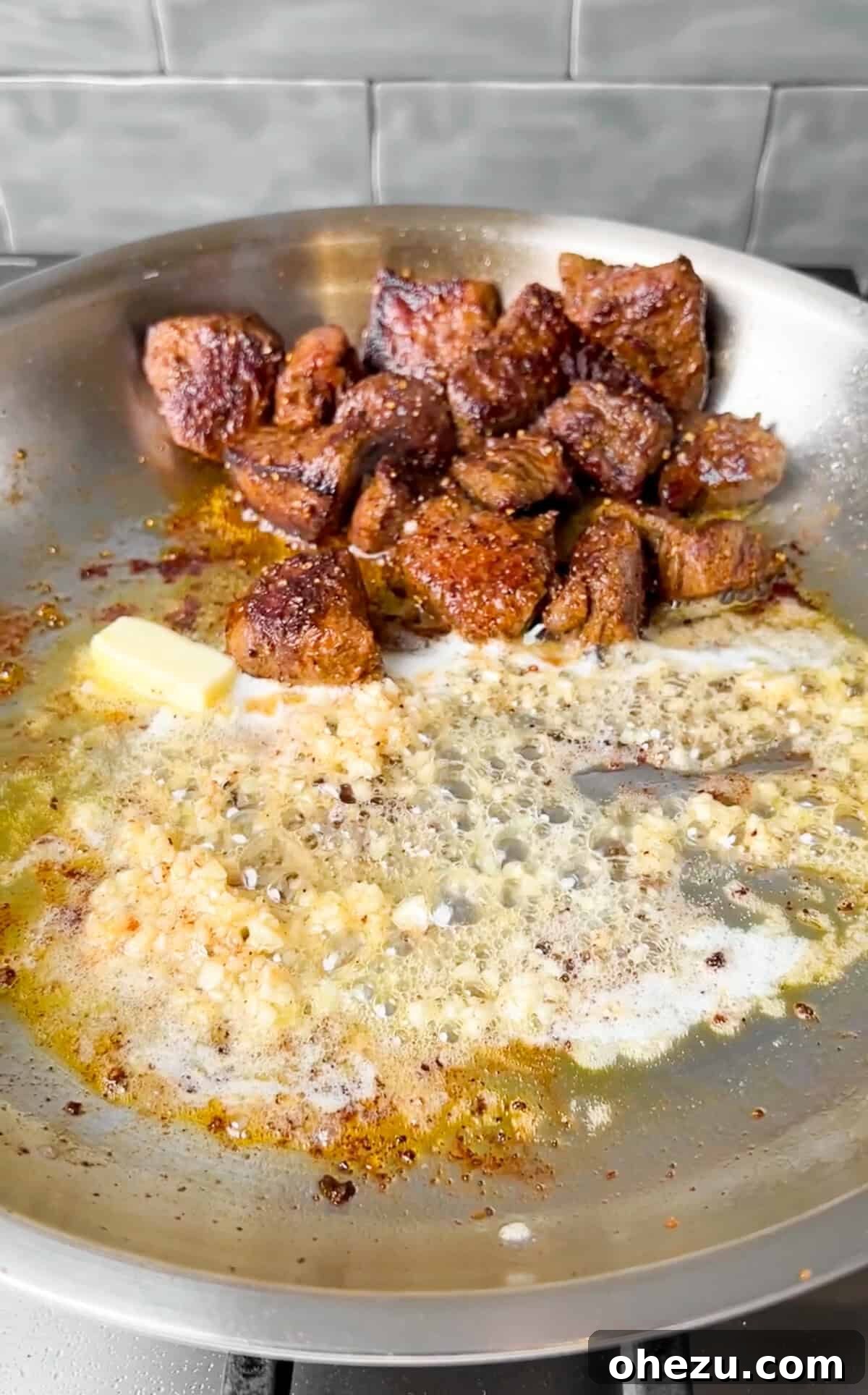 Steak bites being tossed with melted garlic butter in the skillet, coating them in rich flavor.