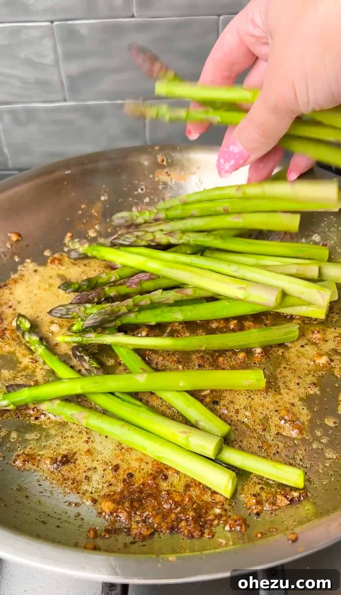 Fresh asparagus spears being added to a buttered pan, ready for sautéing.