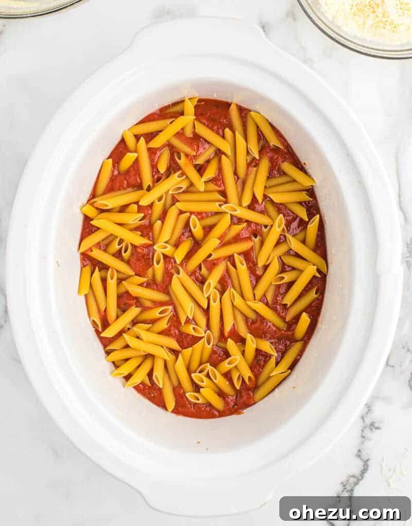 Effortless Slow Cooker Baked Ziti 12 Adding the second section of uncooked penne pasta over the sauce layer.